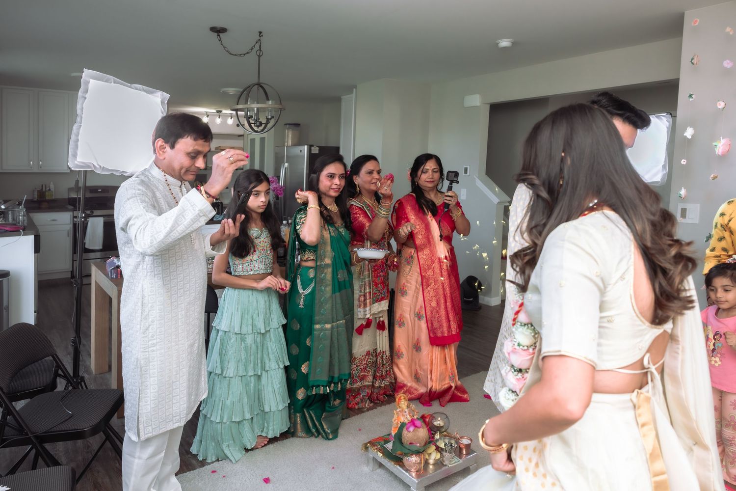 Indian wedding guests in colorful traditional attire gather during pre-wedding ceremony indoors.