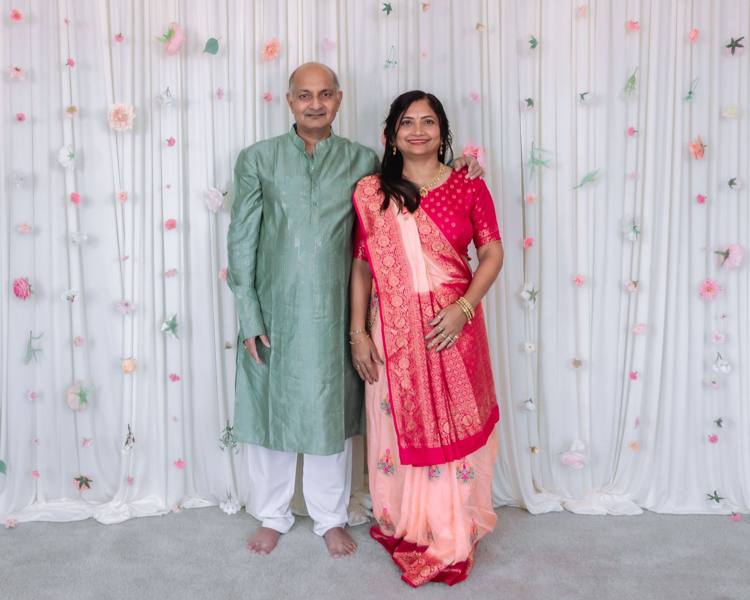Indian couple standing together in traditional attire, man in green kurta and woman in pink saree.