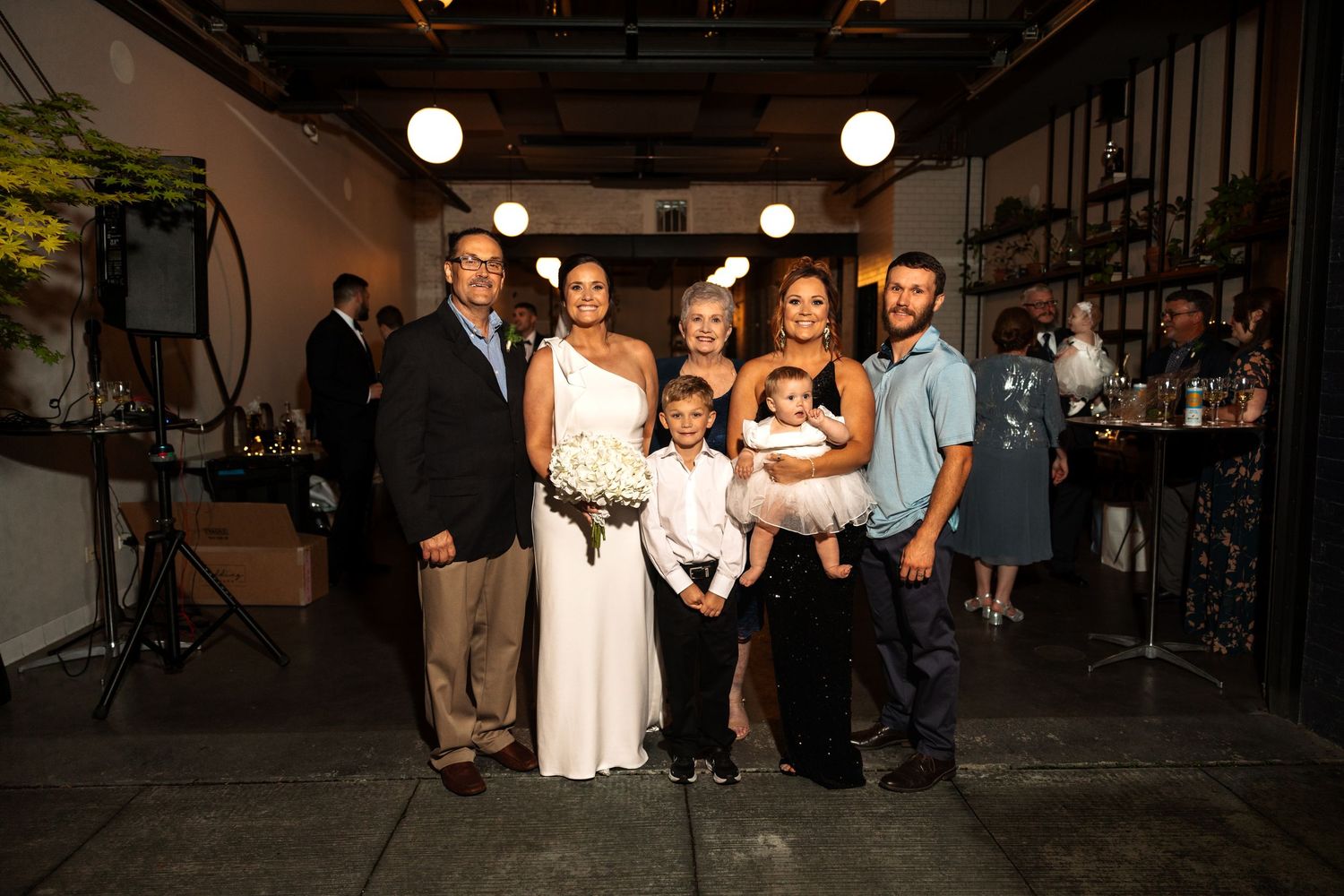 Family group photo with bride holding bouquet at indoor wedding reception venue.