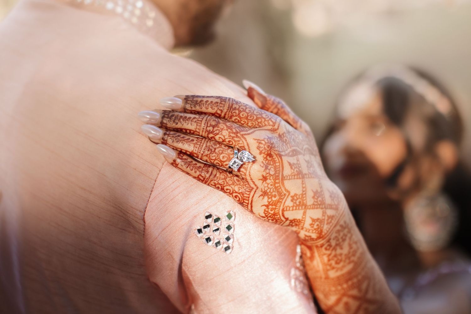 Close-up of intricate henna mehndi design on bride's hand with diamond engagement ring.