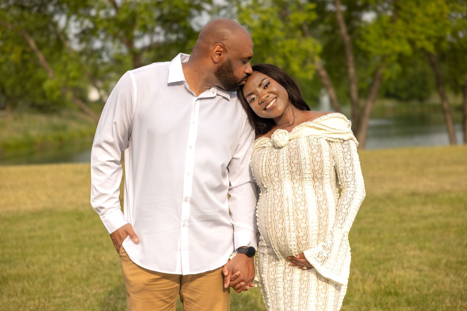 A man kisses his smiling pregnant partner's cheek outdoors.