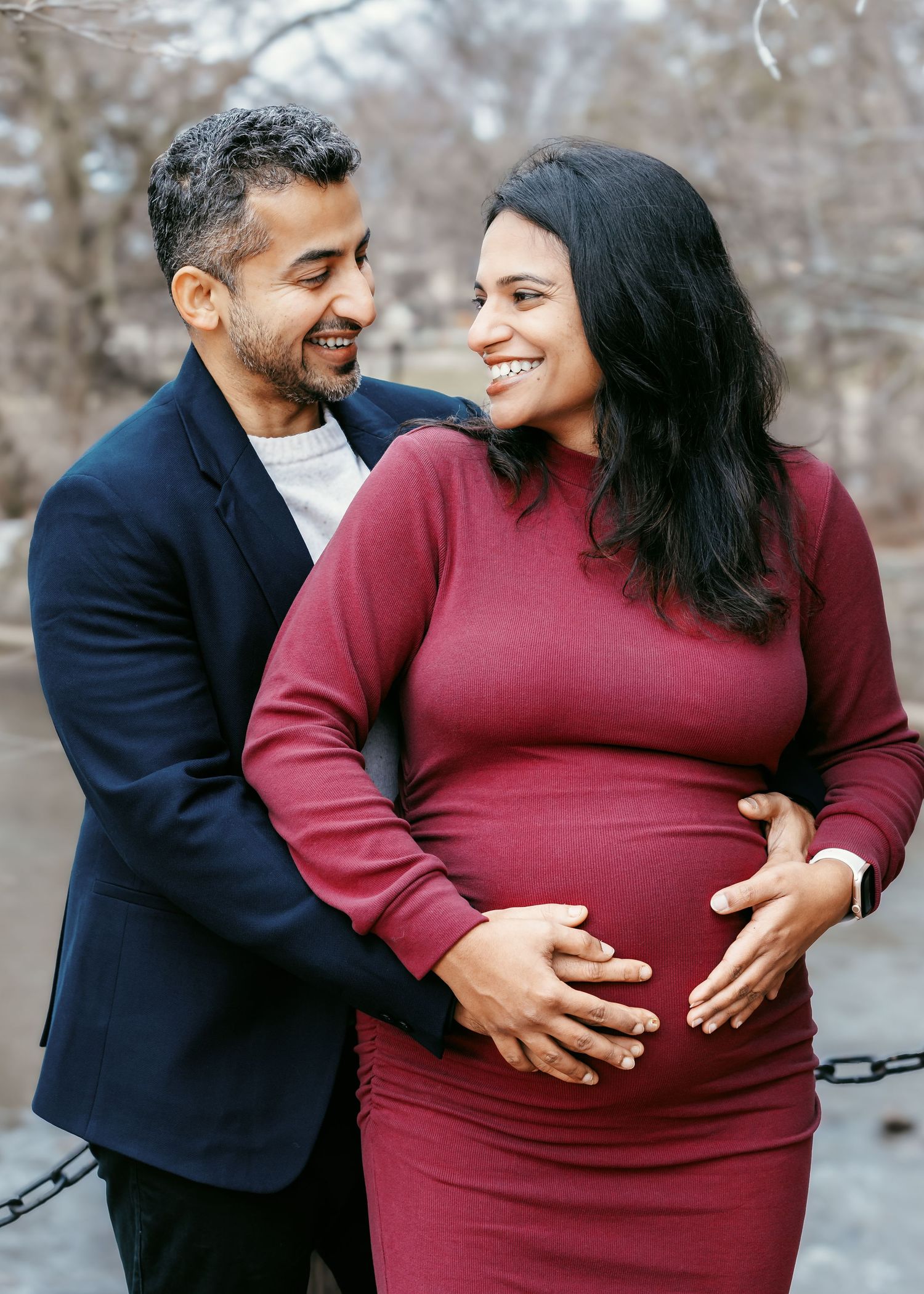 Happy couple at maternity photoshoot, man embracing pregnant woman in burgundy dress.