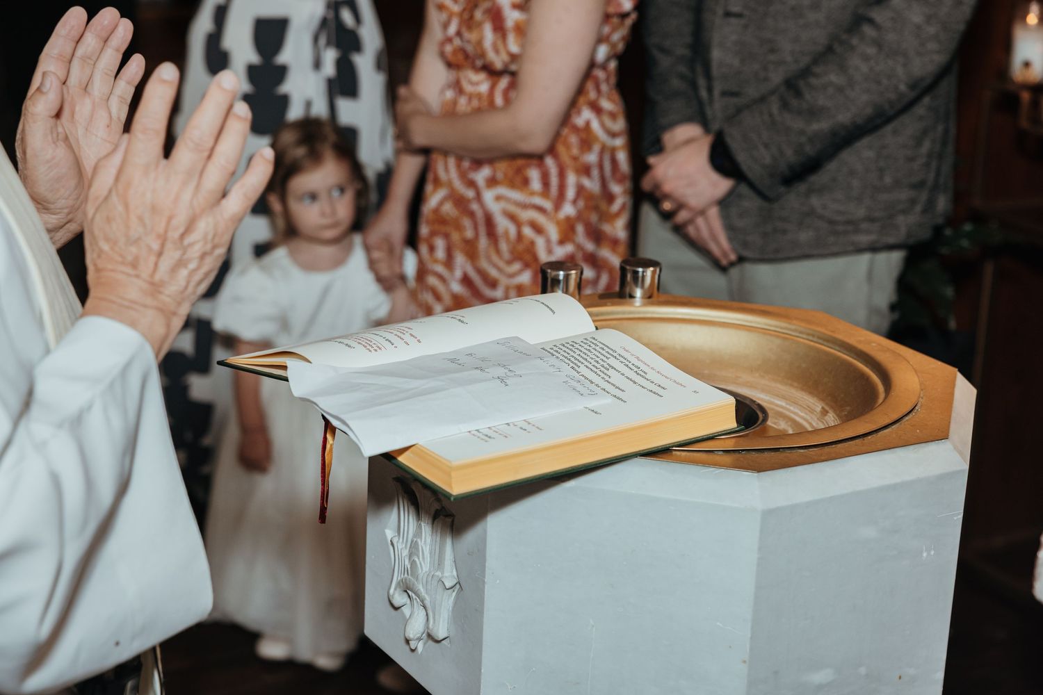 A priest reads from a liturgical book at a golden baptismal font during a Catholic christening.