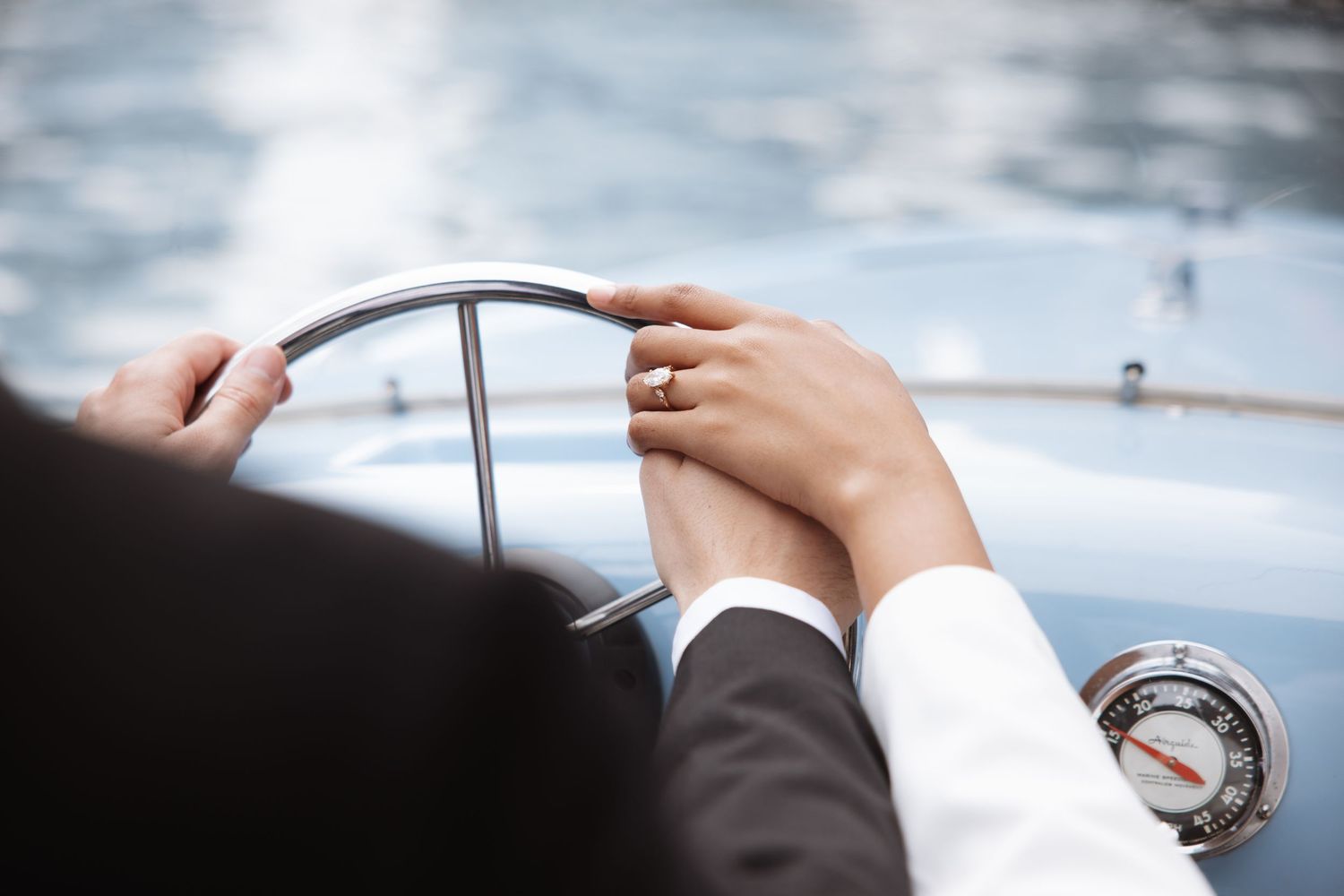 Couple's hands on a vintage boat steering wheel, one wearing a wedding ring, symbolizing romance and togetherness.