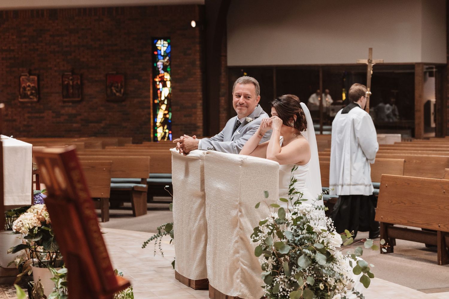 Bride and groom smiling together at the altar during their church wedding ceremony with floral arrangements.