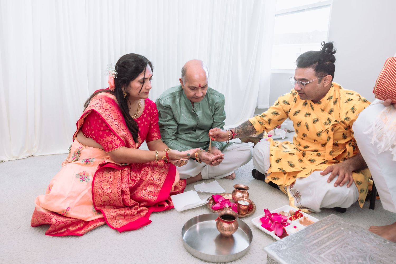 Hindu priest performing traditional ritual with couple seated on floor during Indian wedding ceremony.