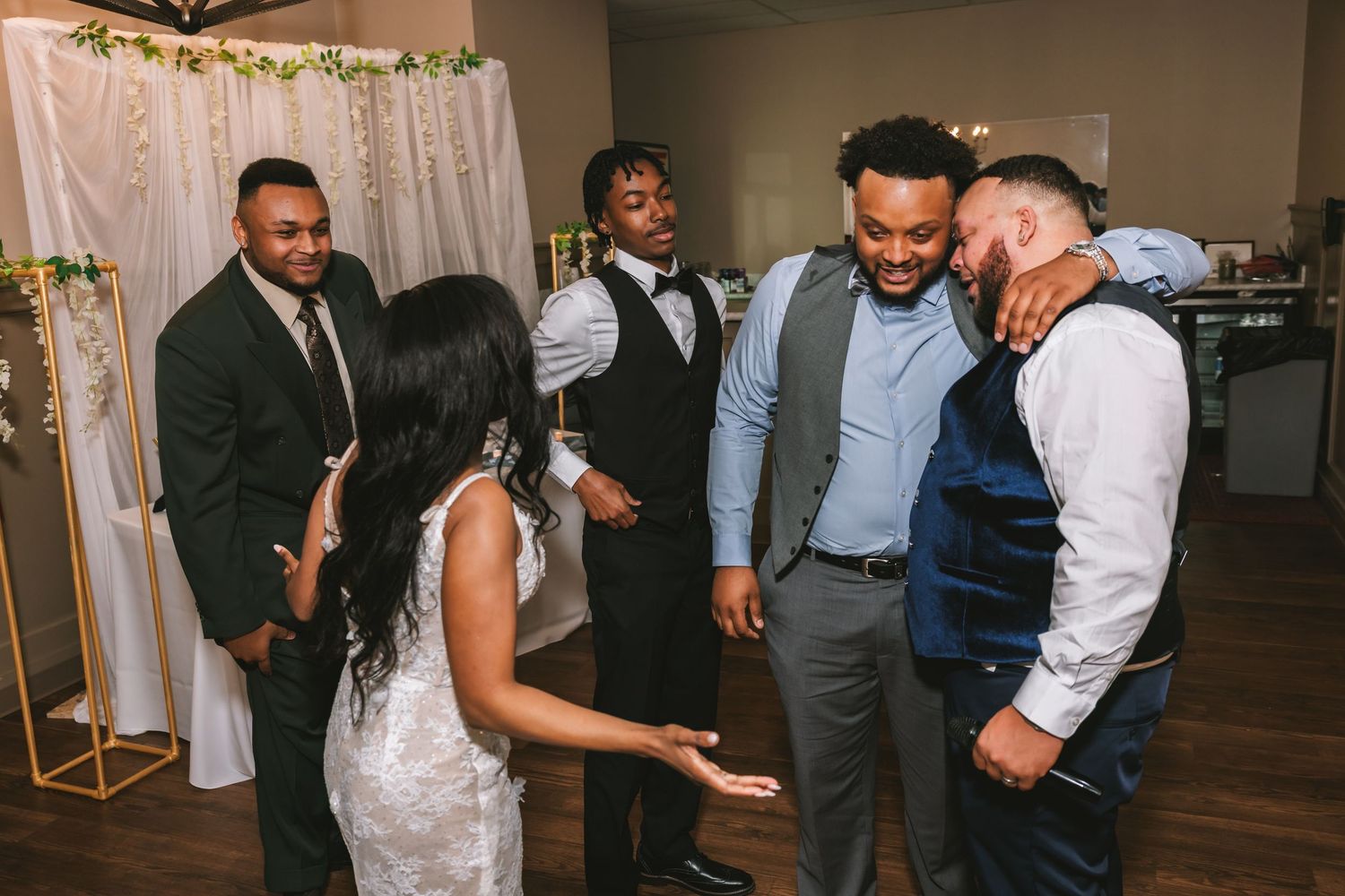Bride and groom sharing joyful moment with groomsmen on wedding reception dance floor.