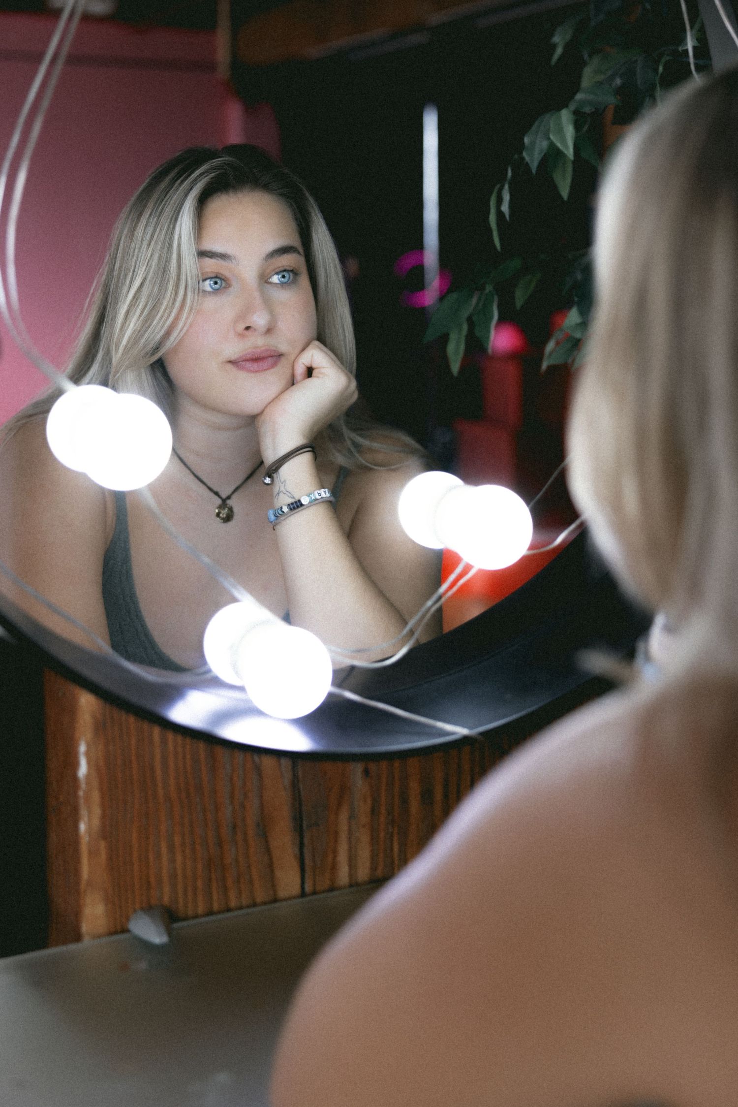 Blonde woman with blue eyes leaning on hand reflected in vanity mirror with Hollywood lights.