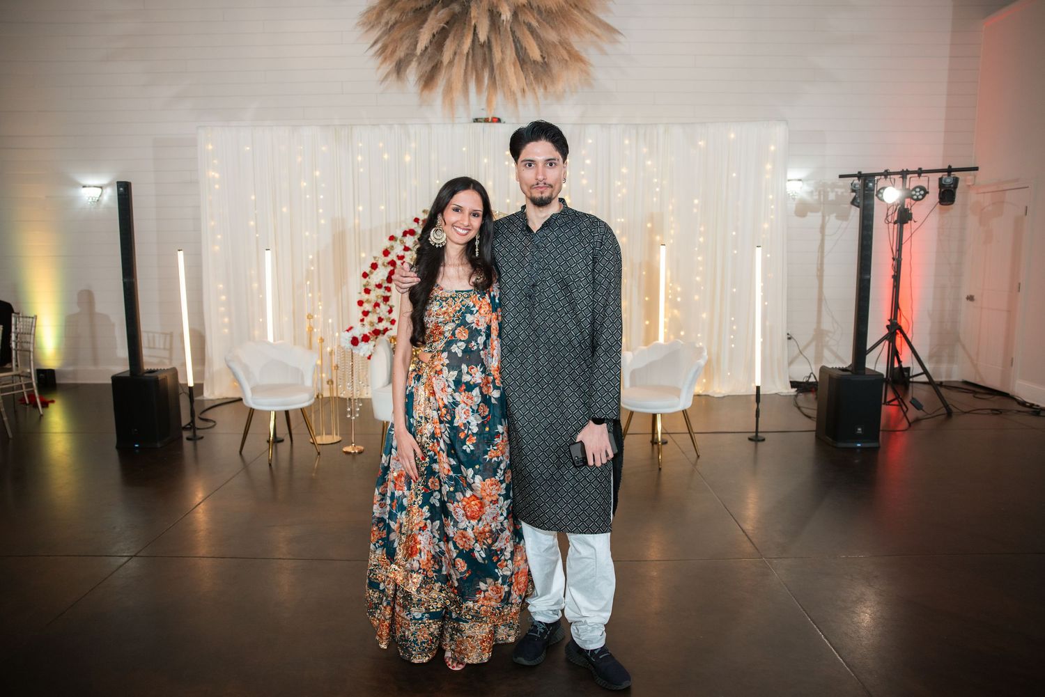 Couple posing elegantly in traditional Indian attire in front of a fairy light backdrop.