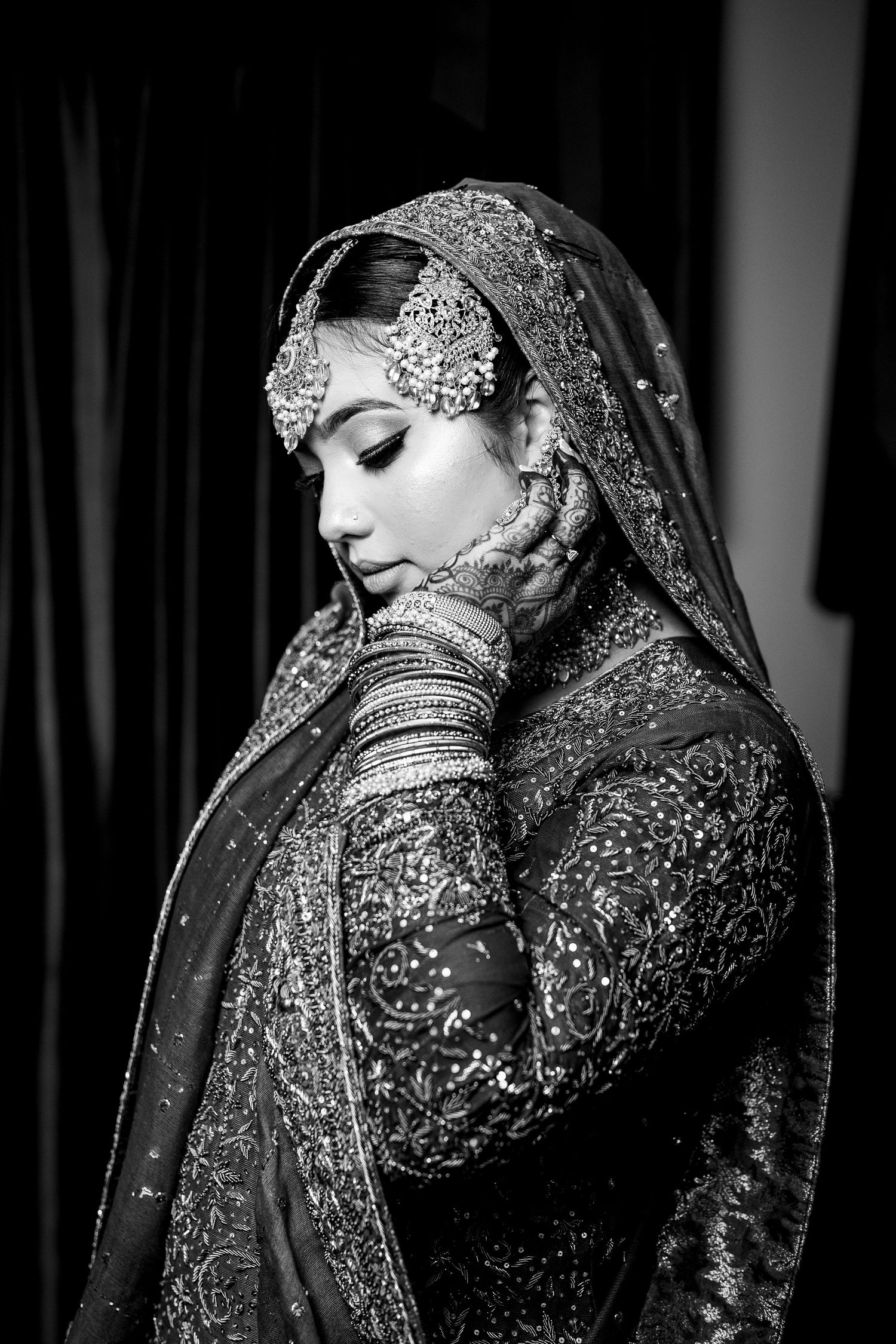 Black and white portrait of Indian bride in embellished lehenga with traditional bridal jewelry and dupatta.