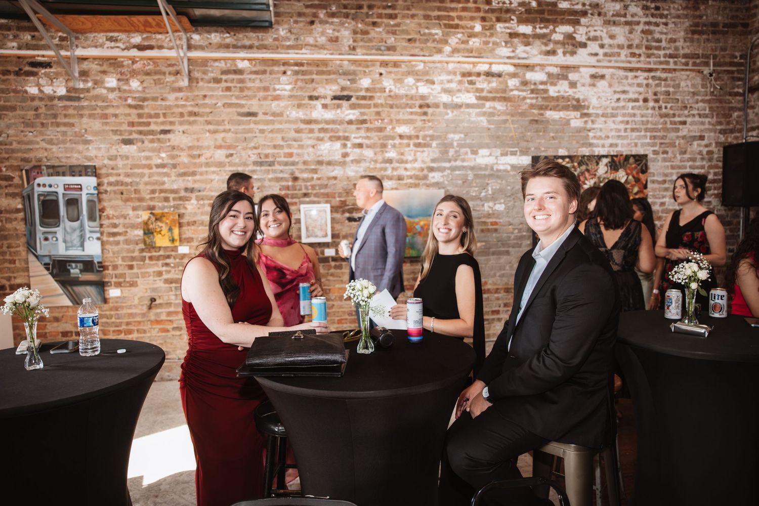 Group of guests smiling at a table during a festive event in a brick-walled venue.
