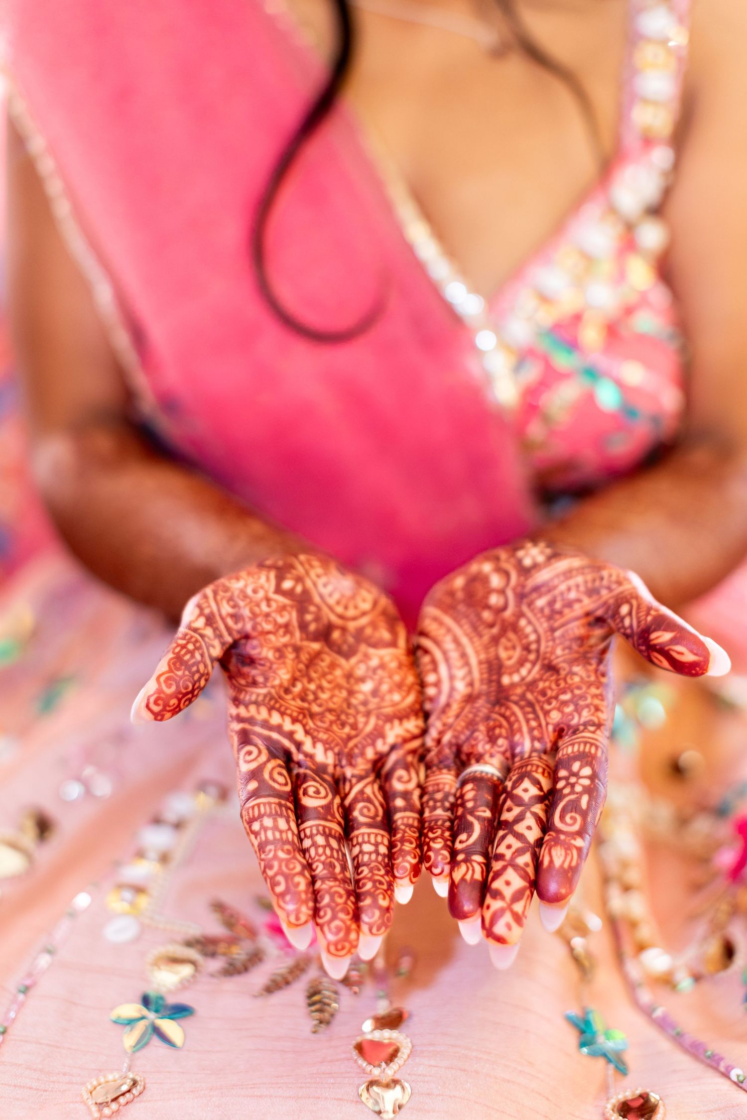 Indian bride showing detailed henna mehndi patterns on cupped palms in pink saree.