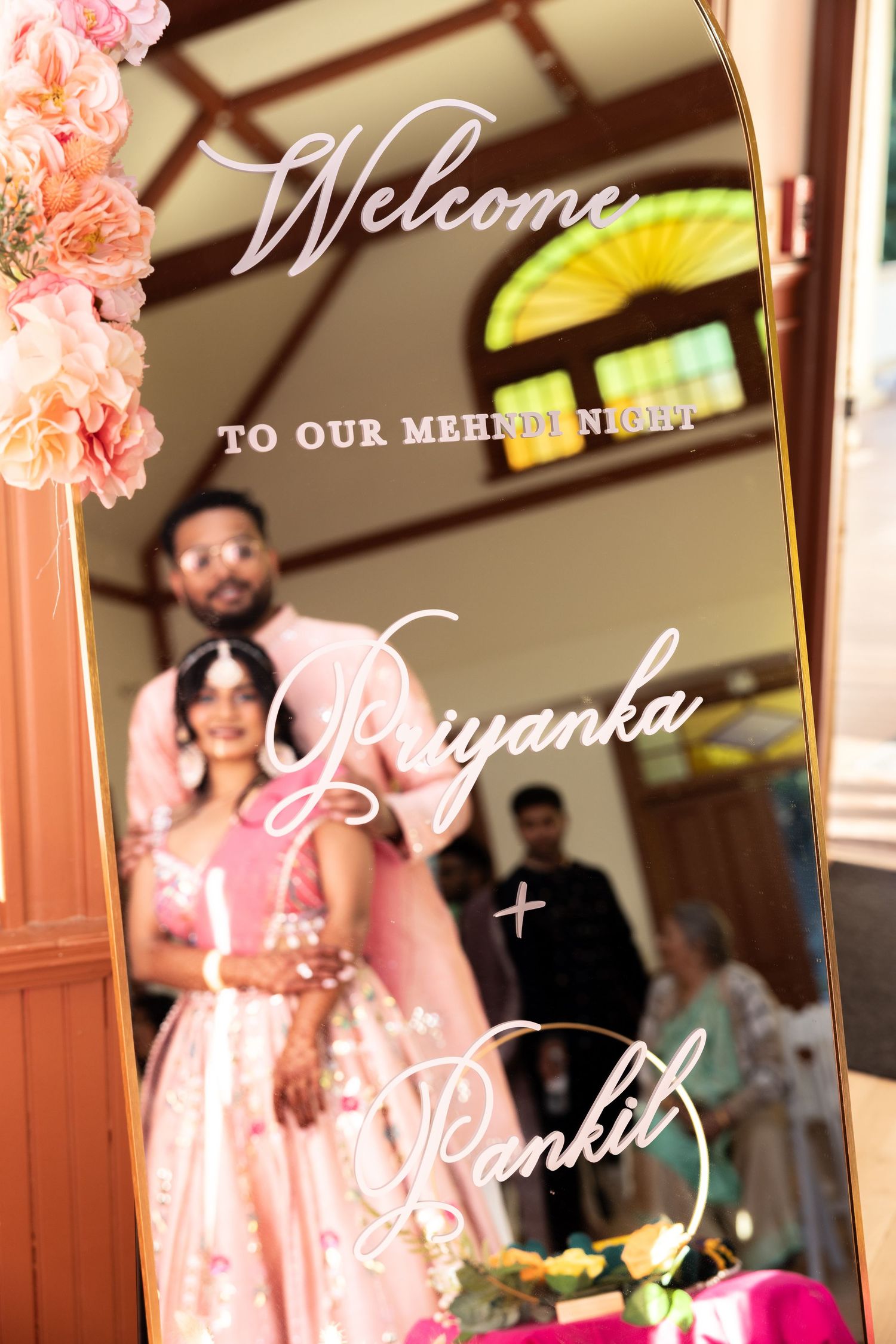 Welcome mirror sign for Priyanka and Pankil mehndi night celebration with couple reflected behind.