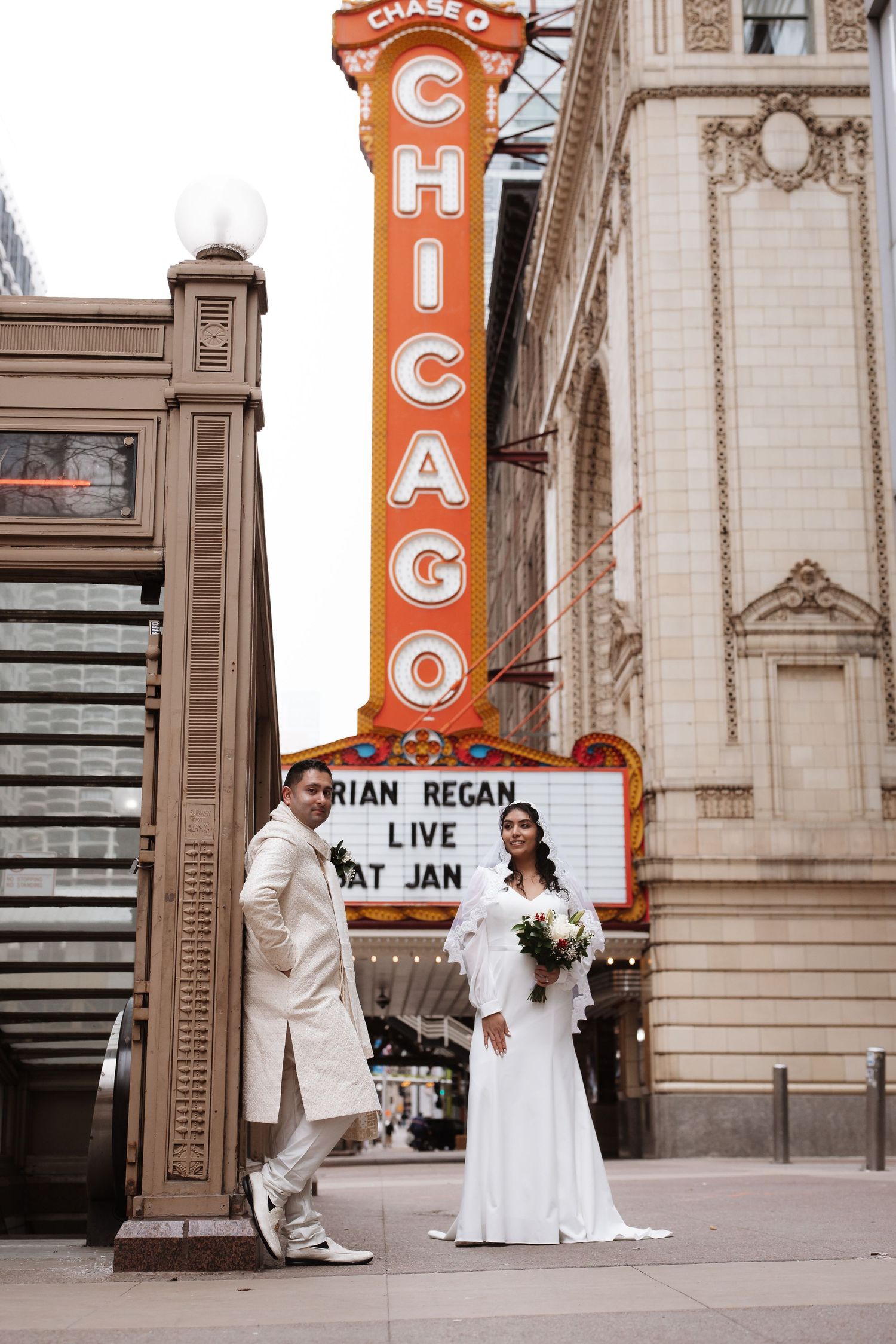 Bride and groom standing apart near Chicago Theatre marquee on their wedding day.