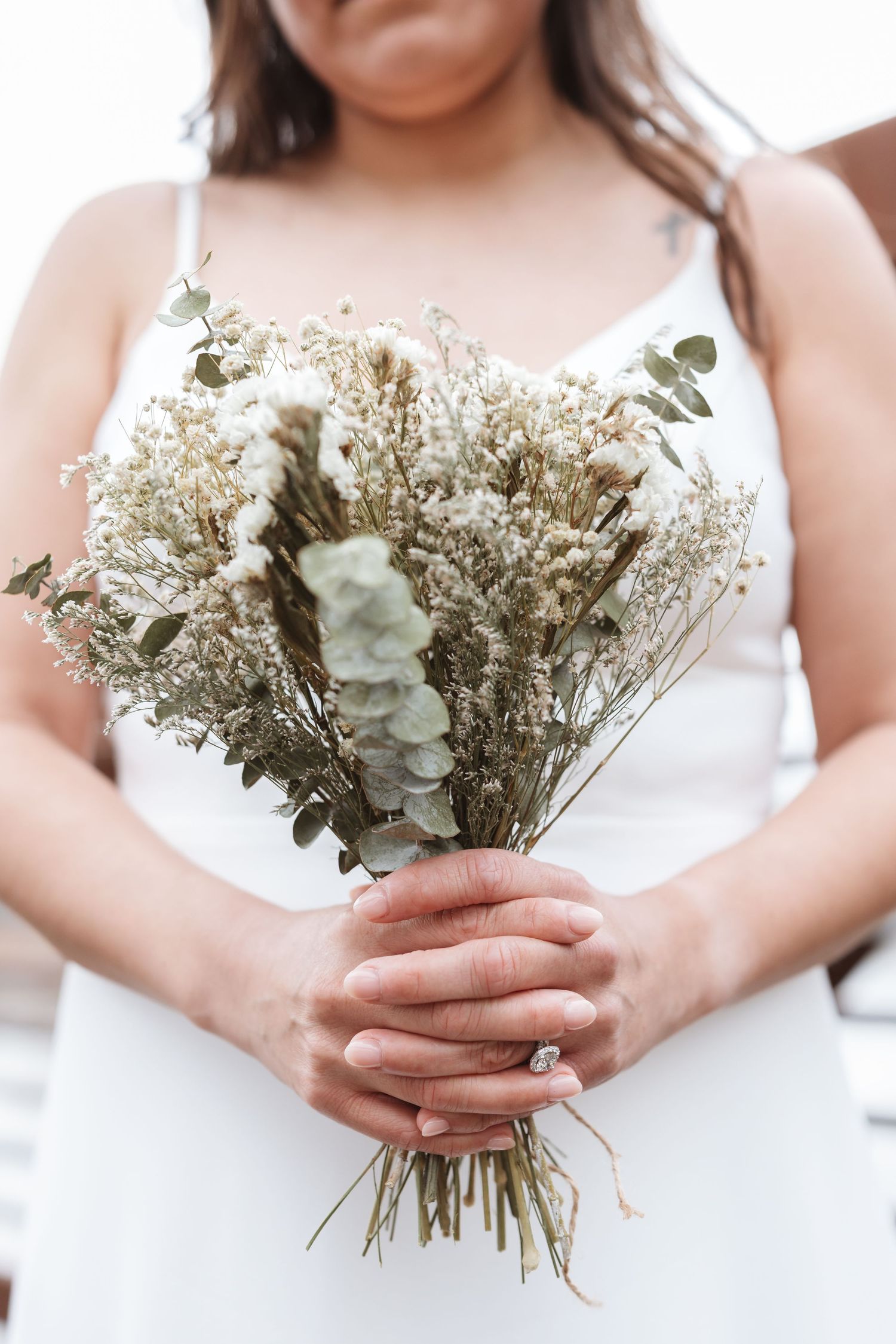 Bride in white dress holding a rustic dried flower bouquet with eucalyptus, wearing a diamond ring.