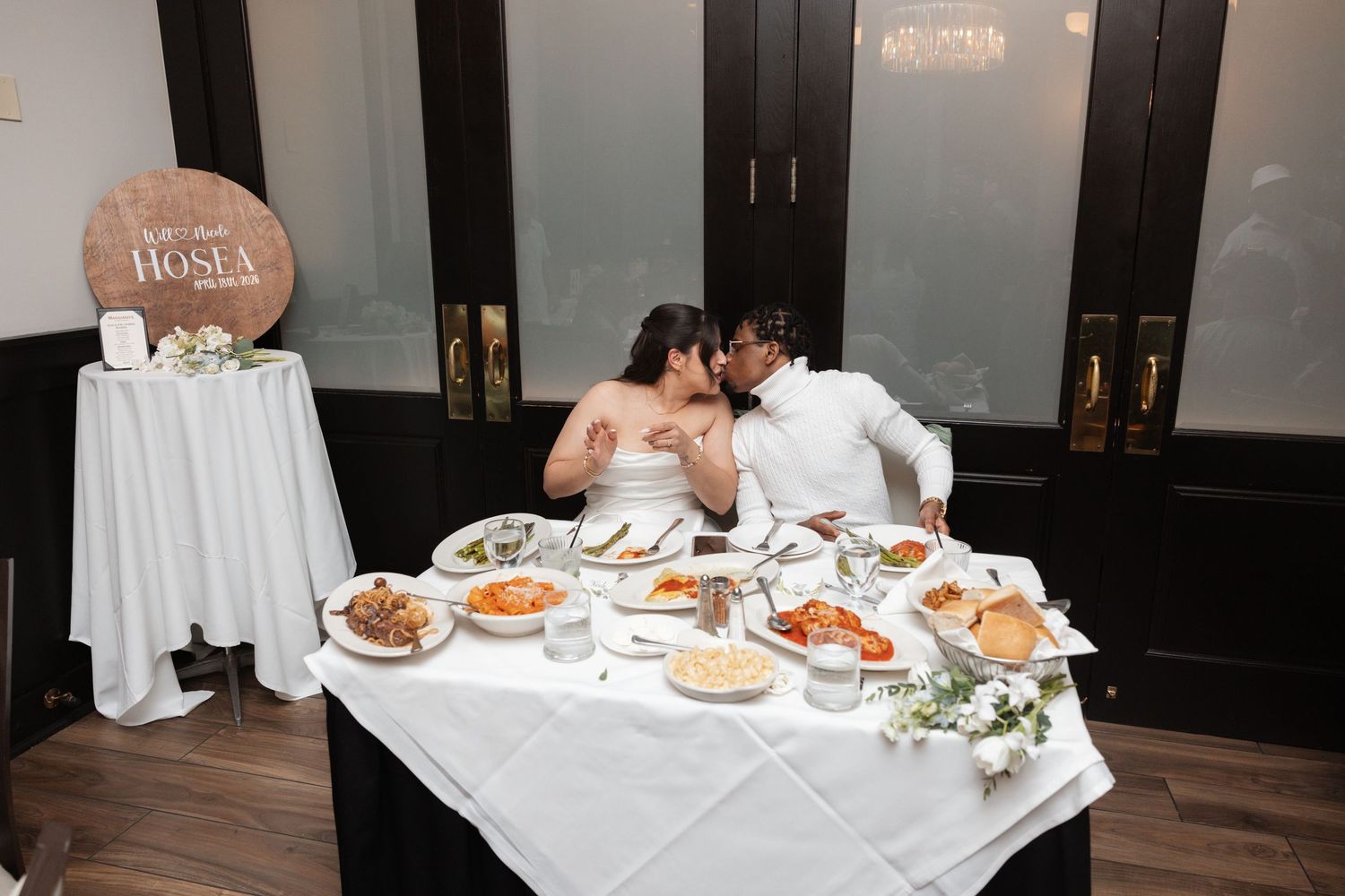 Bride and groom sharing a kiss at their sweetheart table during wedding reception.