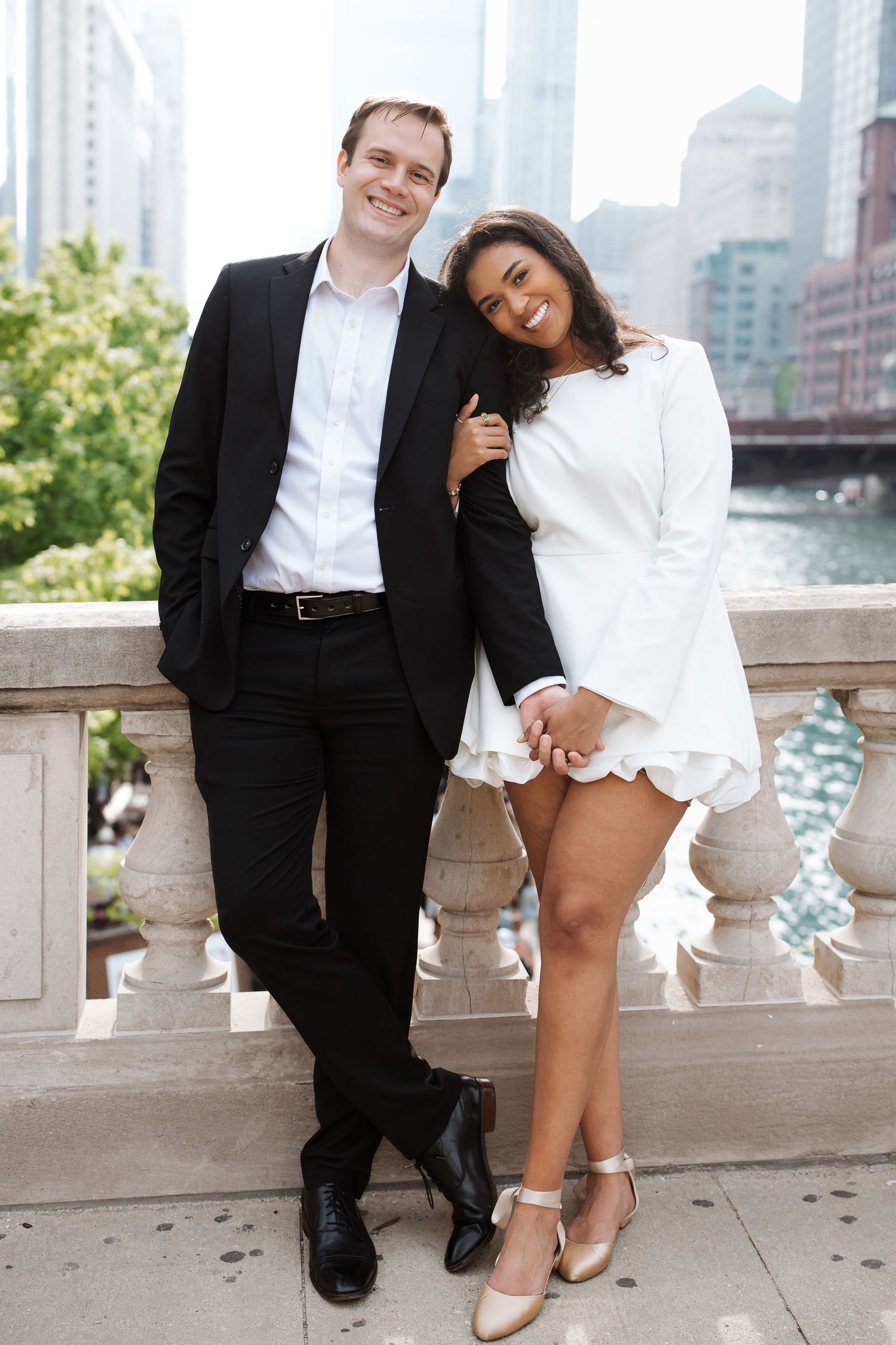 Smiling couple posing on a Chicago riverside terrace with skyline and river behind them.