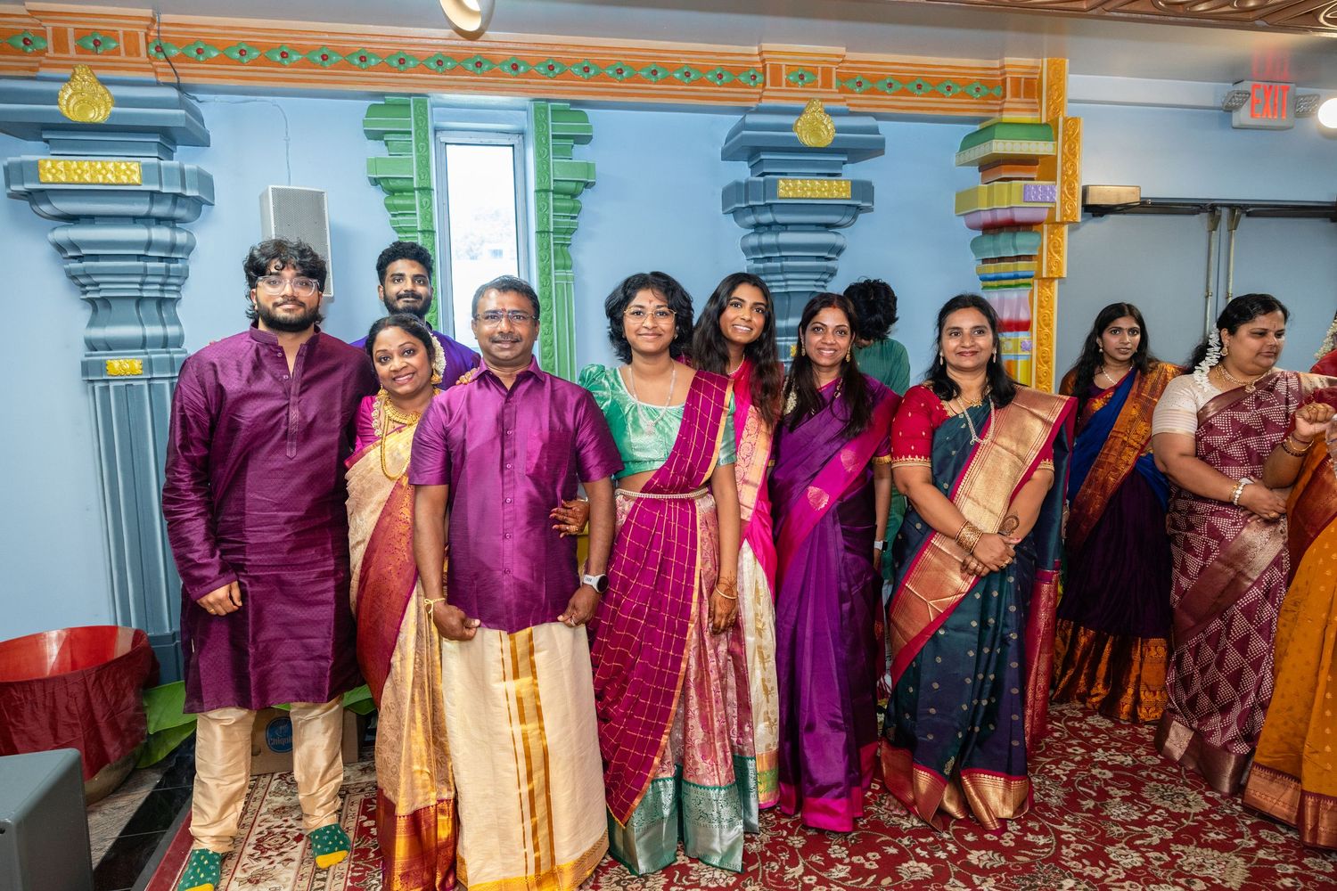 South Indian family group photo in vibrant traditional silk sarees and kurtas at a Hindu temple.