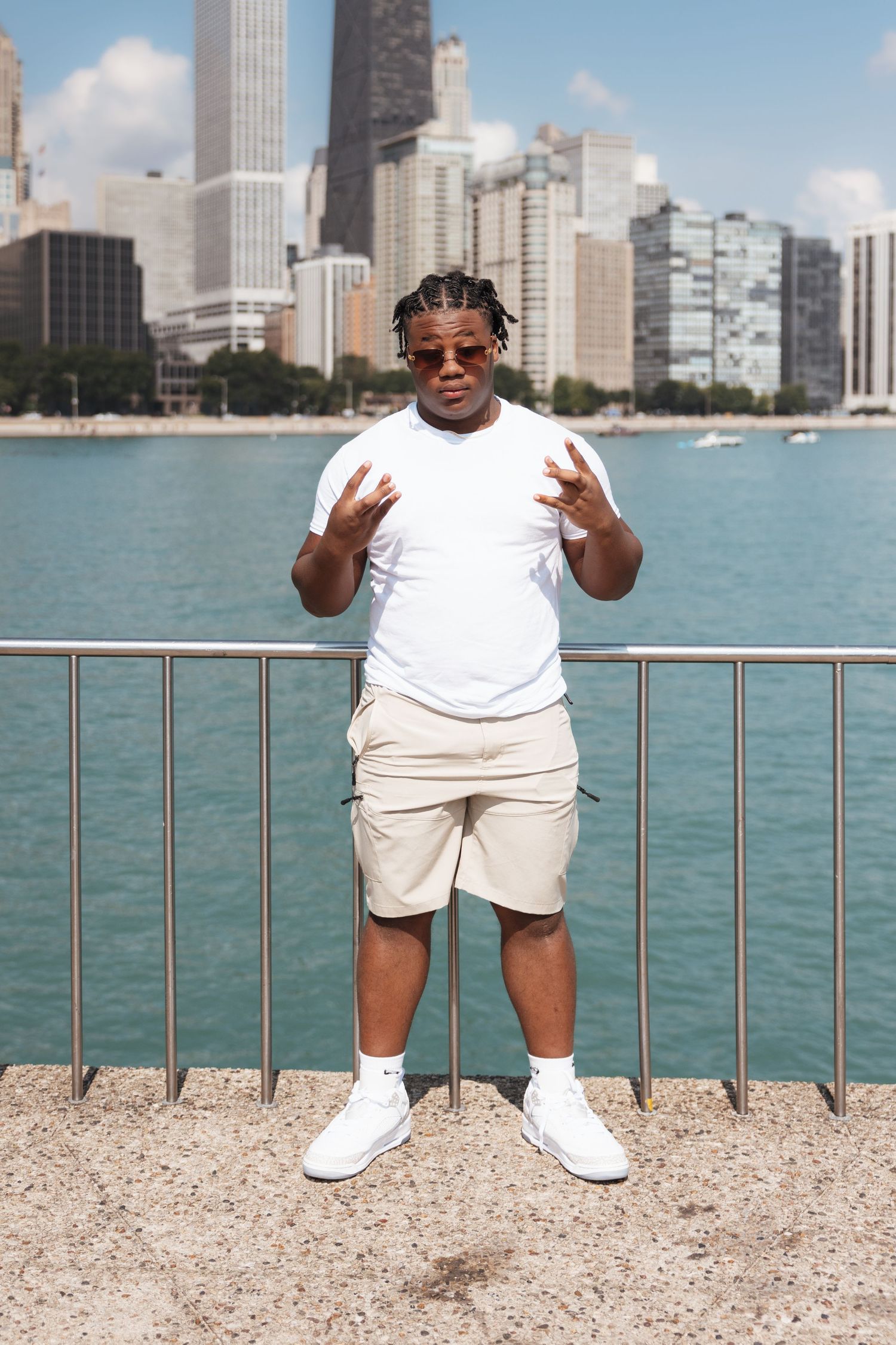 Man in white outfit and sunglasses posing confidently by Chicago lakefront skyline on sunny day.