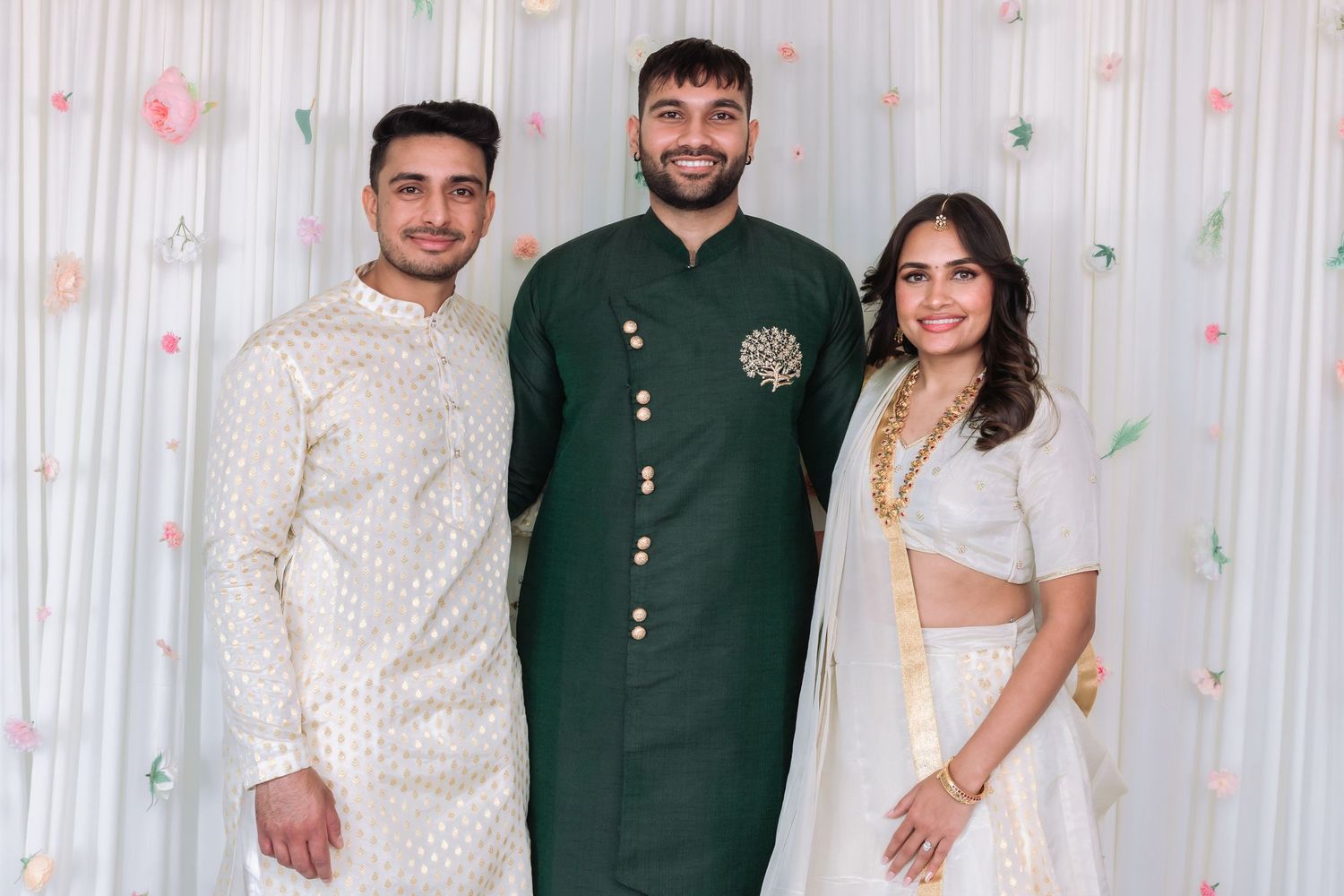 Three young men and woman posing at Indian celebration in traditional white and green outfits.