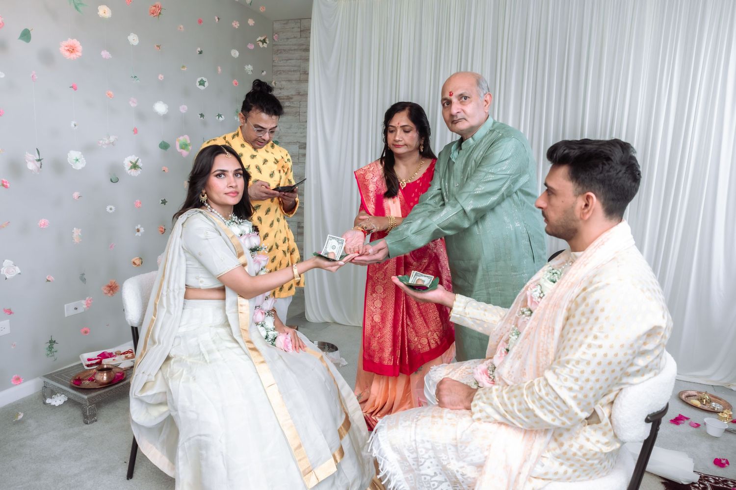 Family members perform a traditional Hindu wedding ritual with bride in white and groom in cream attire.
