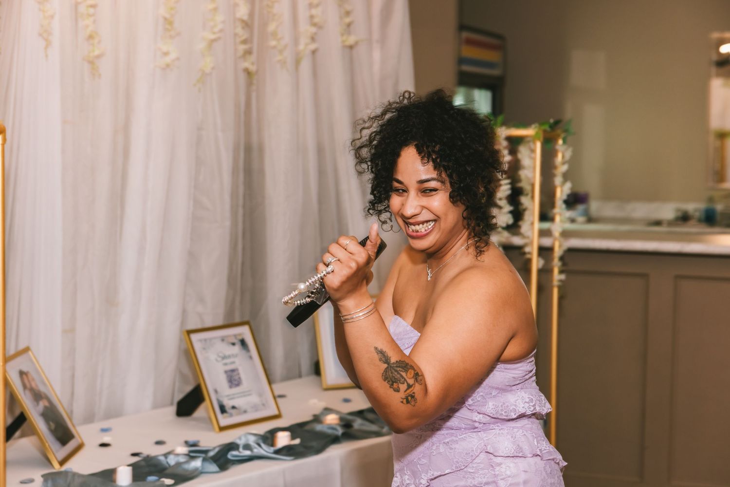 Woman in lavender dress smiling while holding a microphone at a wedding reception.