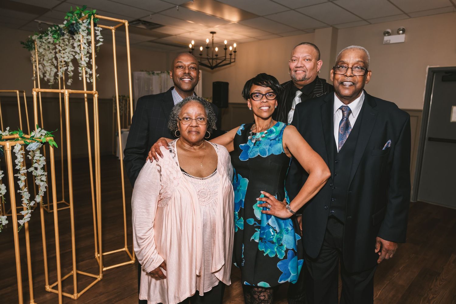 Group of five wedding guests posing together in front of gold geometric floral display.