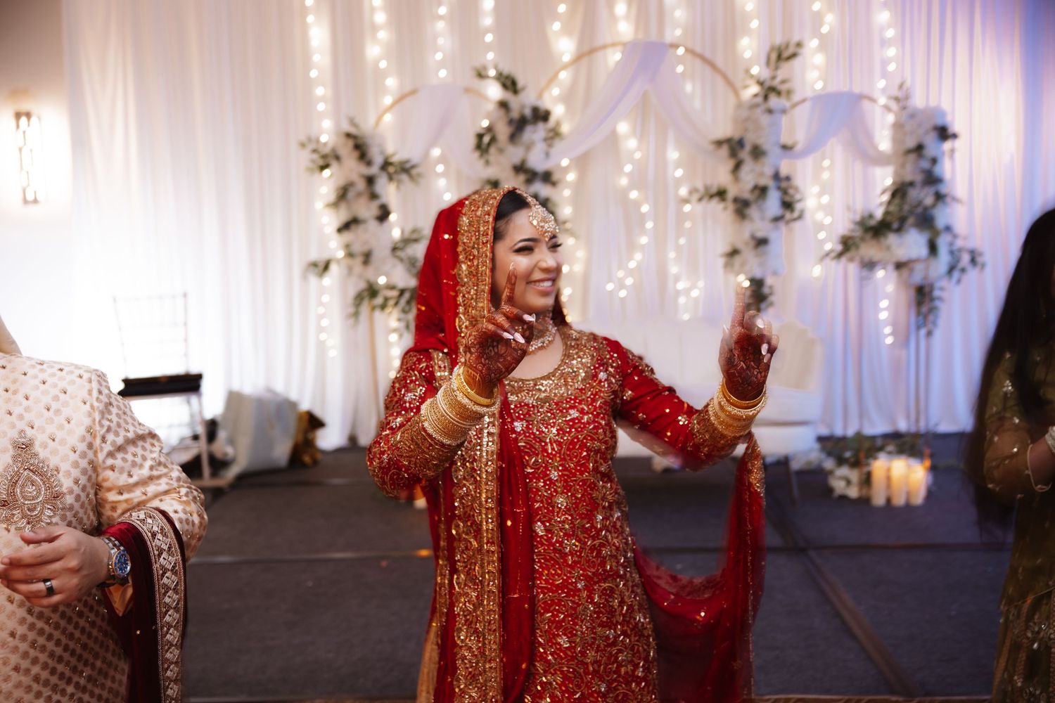 Indian bride in red and gold bridal lehenga dancing joyfully at wedding reception celebration.