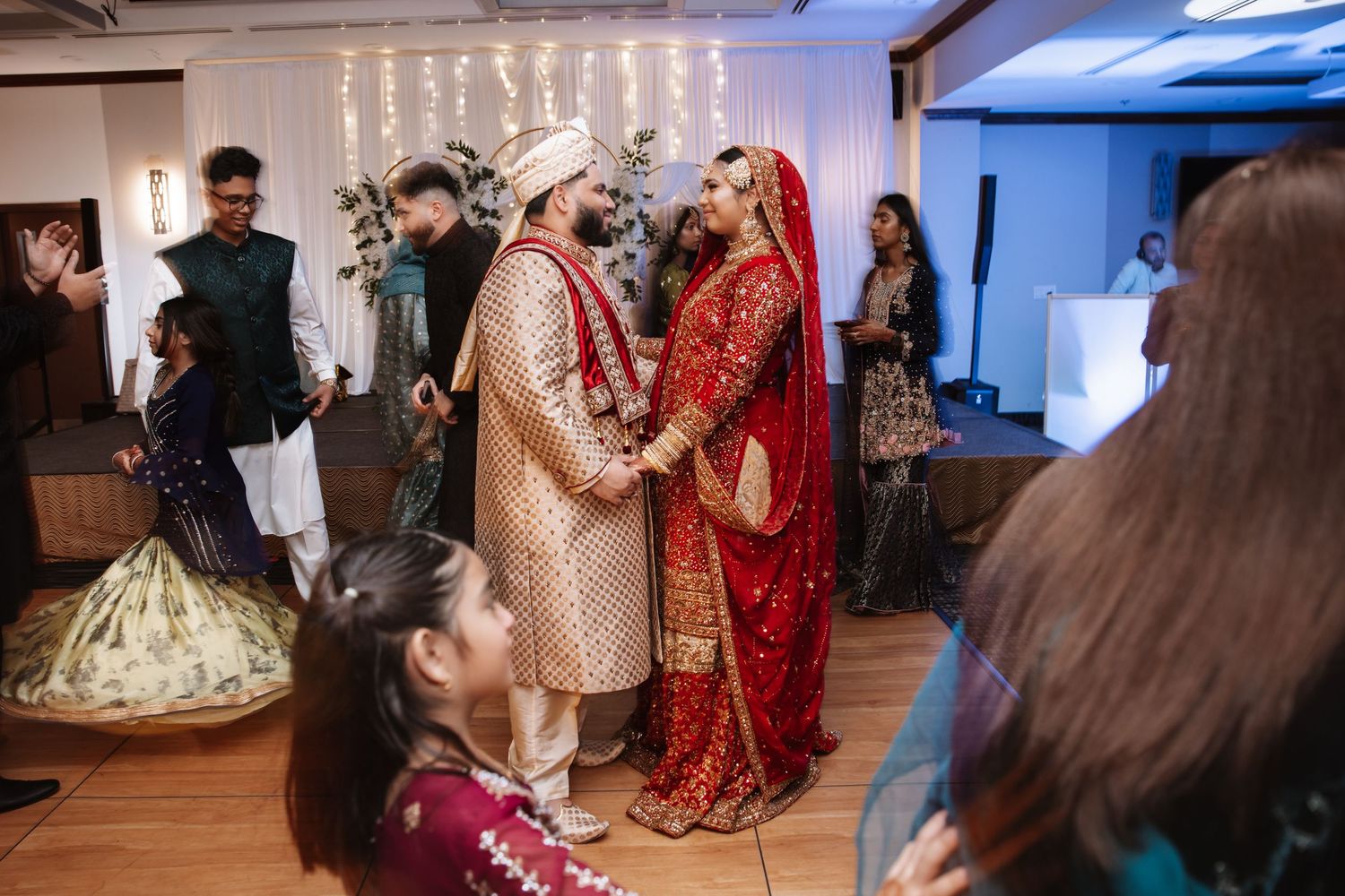 Bride and groom in traditional South Asian wedding attire holding hands at ceremony.