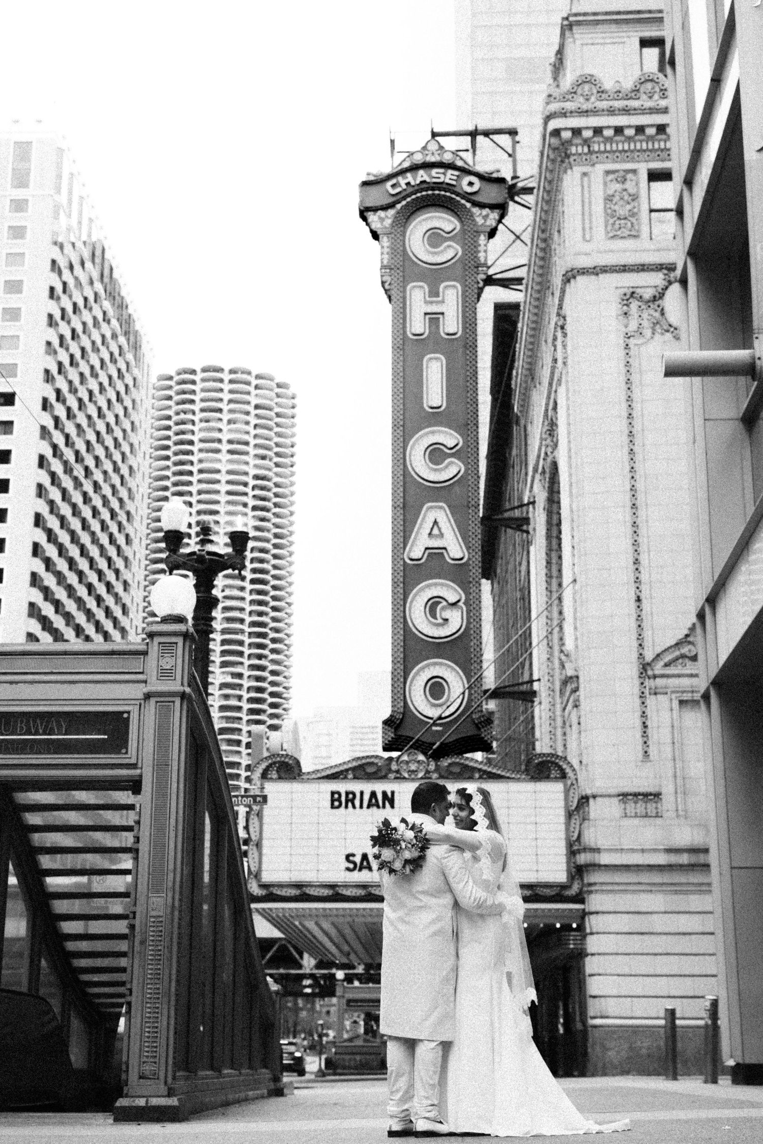 Black and white photo of newlyweds embracing in front of the Chicago Theatre sign.