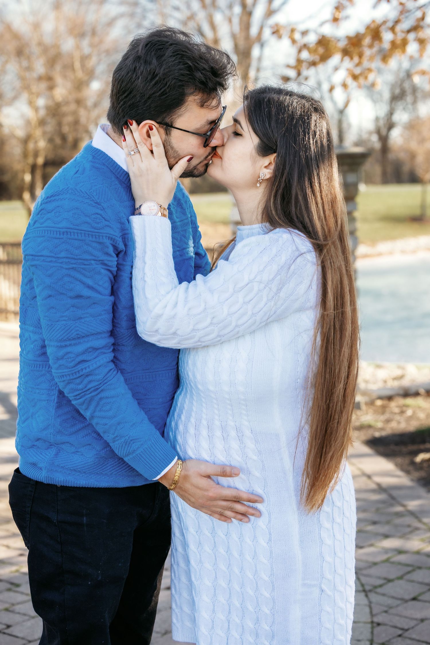 Loving couple sharing a kiss outdoors during maternity photoshoot, man cradling pregnant belly.