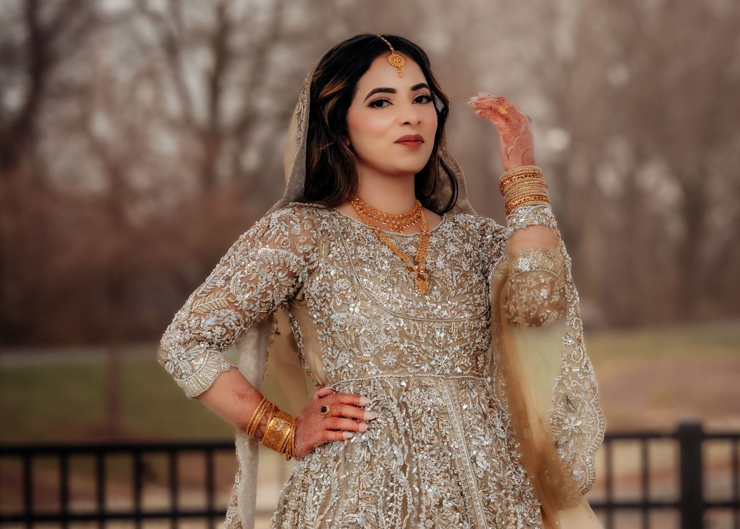 Bride in ornate gold embroidered South Asian bridal lehenga with jewelry posing outdoors.