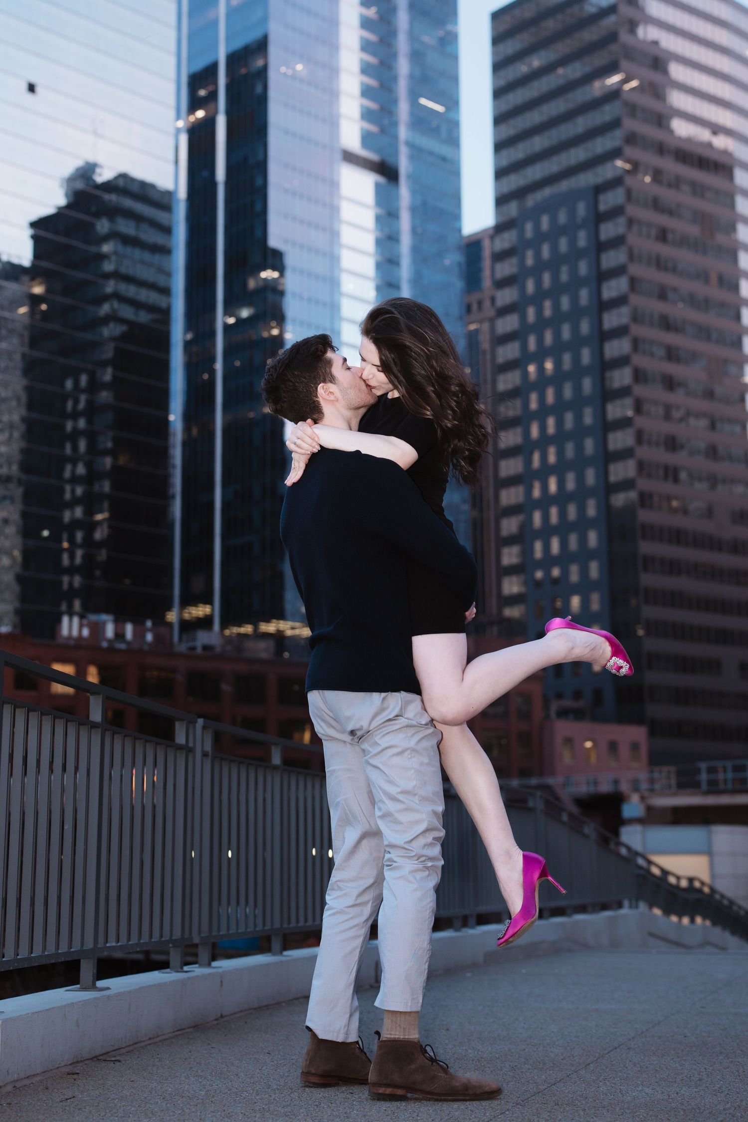 A man lifts and kisses his partner against a dramatic Chicago city skyline at dusk.