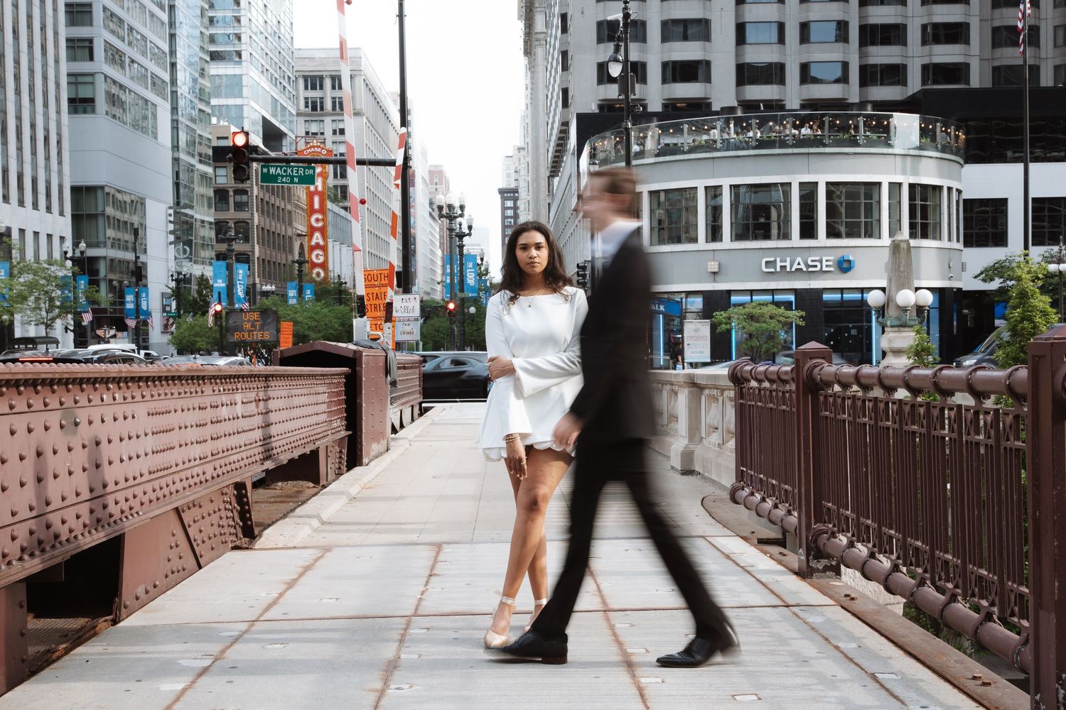 Woman in white dress on Chicago bridge with blurred businessman walking past her.
