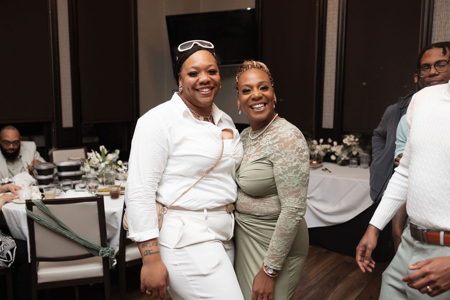 Two women smiling and posing together at an elegant wedding reception in formal attire.