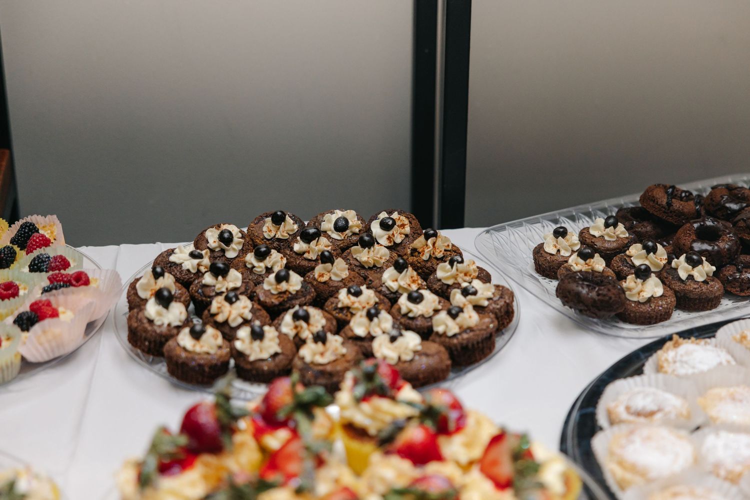Elegant wedding dessert table featuring chocolate cupcakes with cream, fruit tarts, and powdered donuts.
