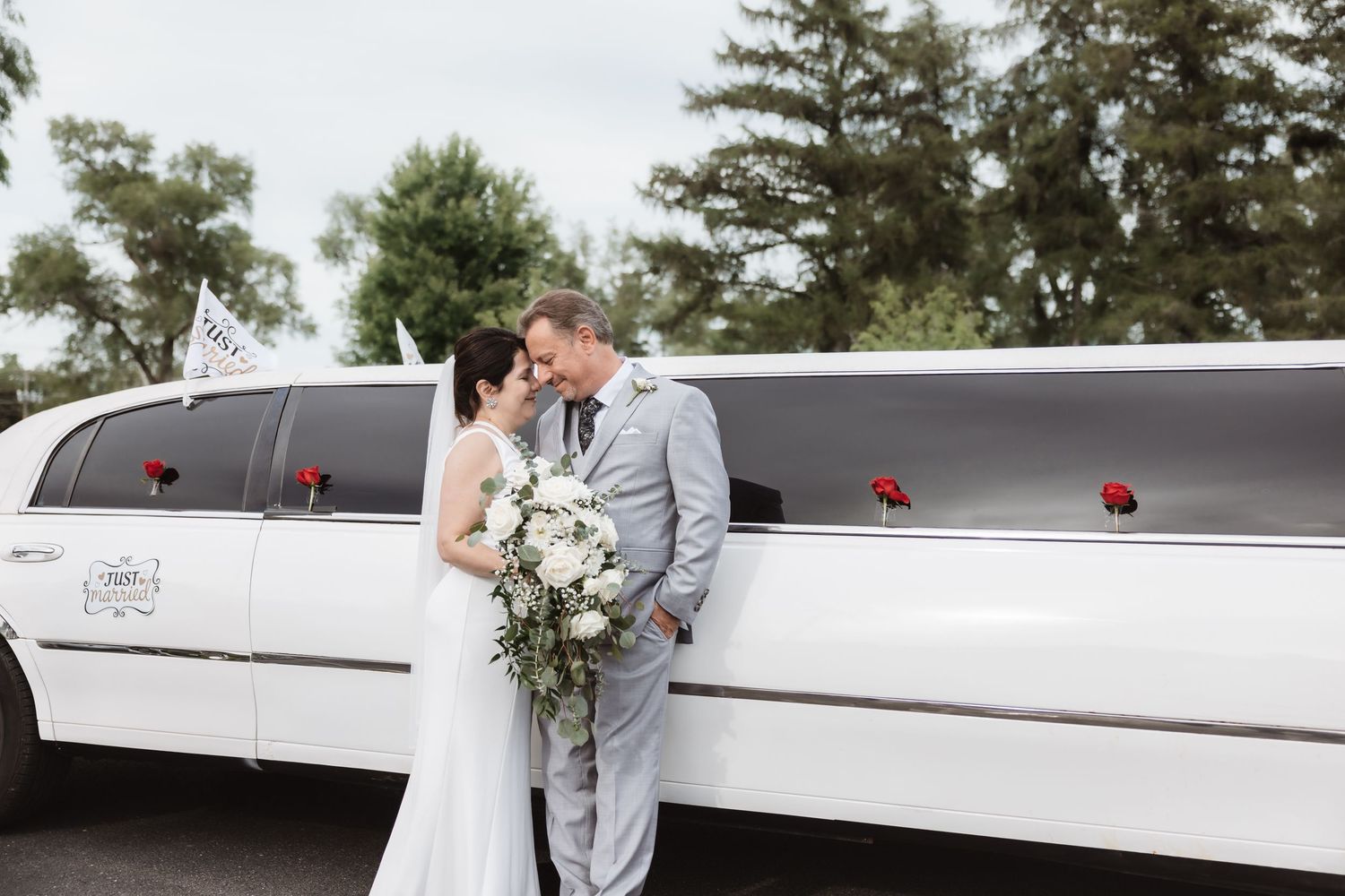 Bride and groom share a romantic moment in front of a white stretch limousine outdoors.