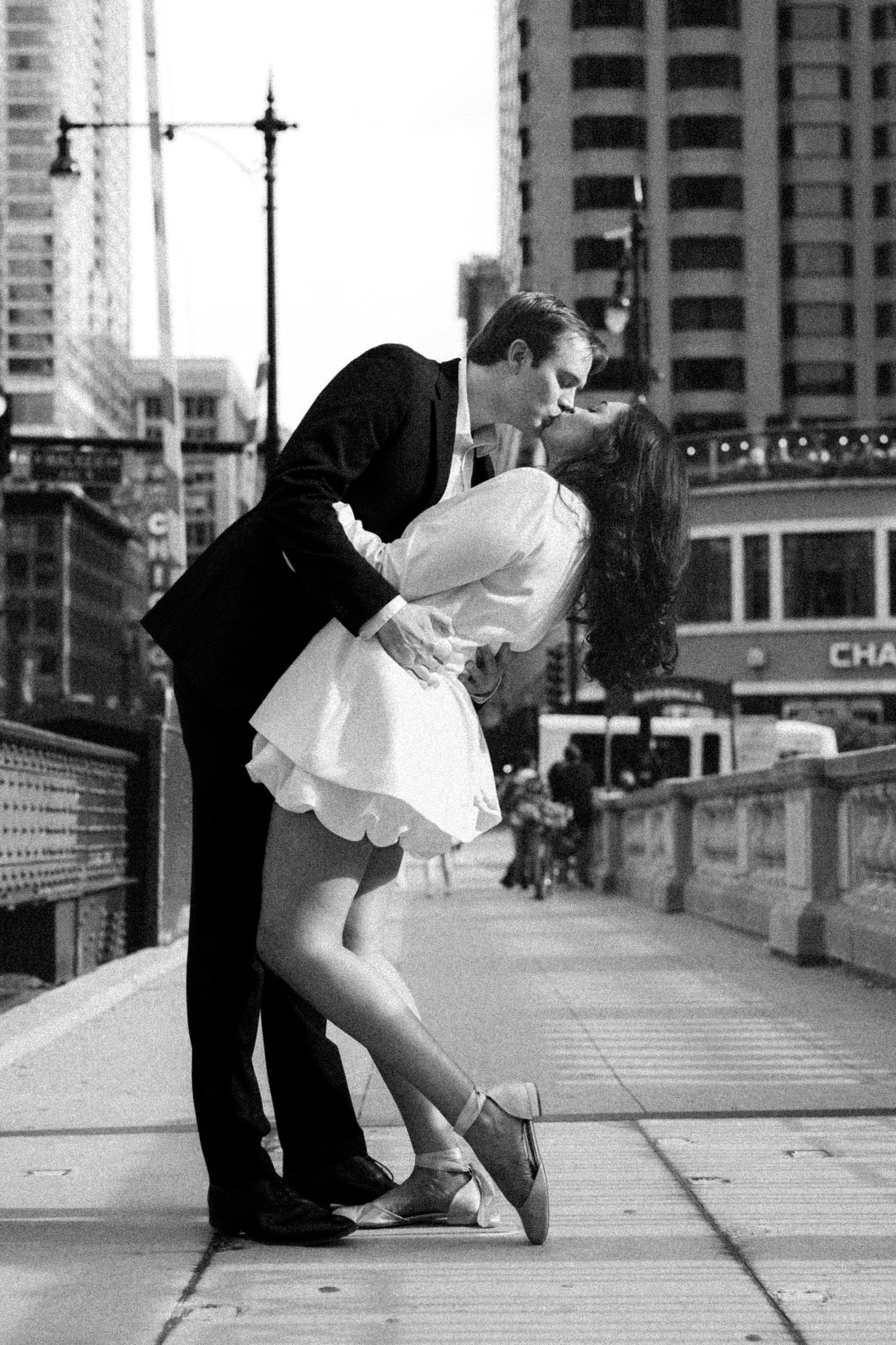 Black and white photo of couple sharing romantic dip kiss on urban city bridge.