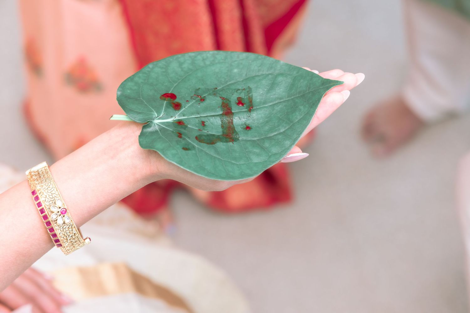 Hand holding green betel leaf with sacred Hindu Om symbol written in red kumkum during wedding ritual.
