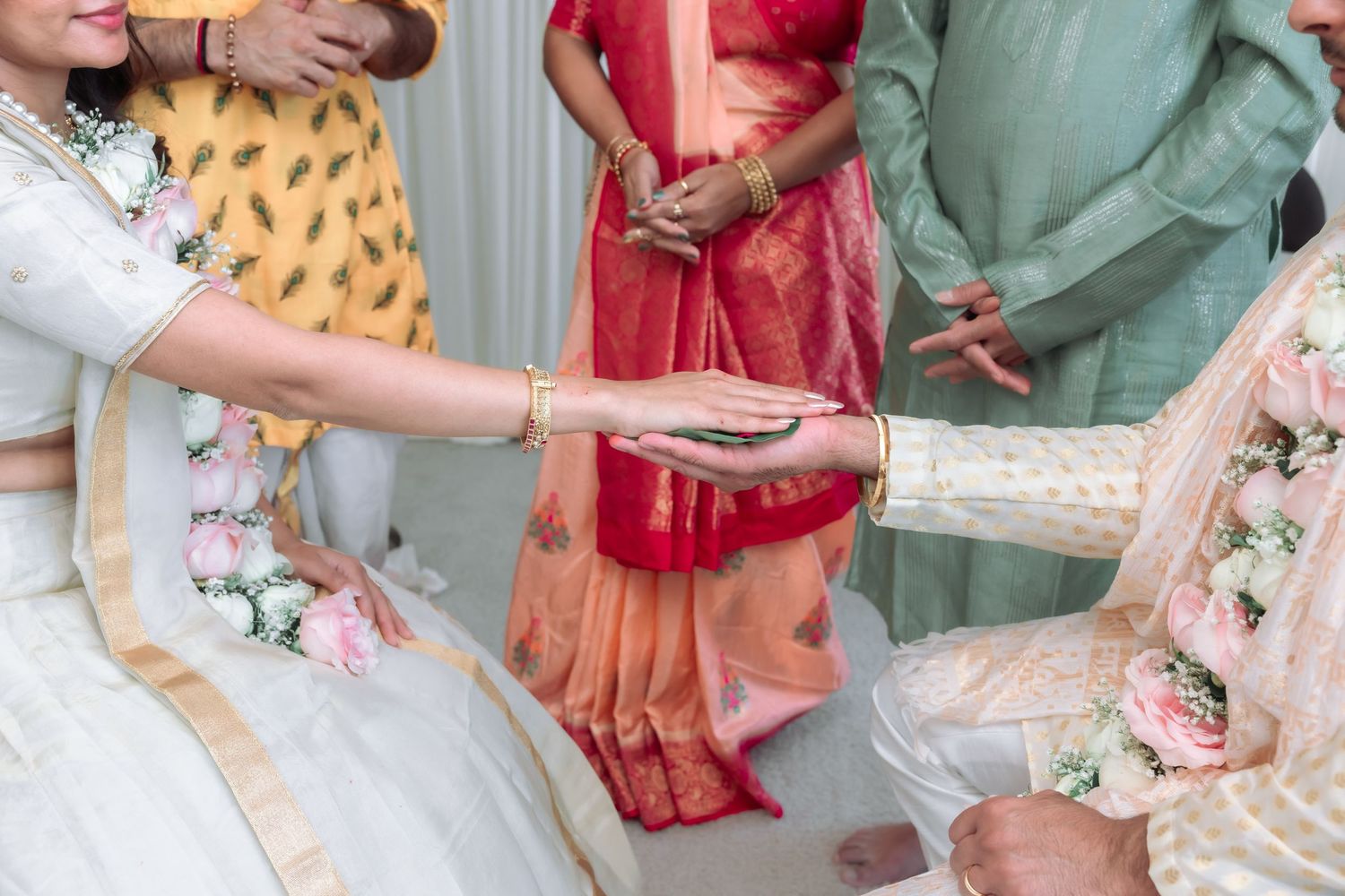 Bride in white lehenga extends her hand during a traditional Hindu wedding ceremony ritual with family.