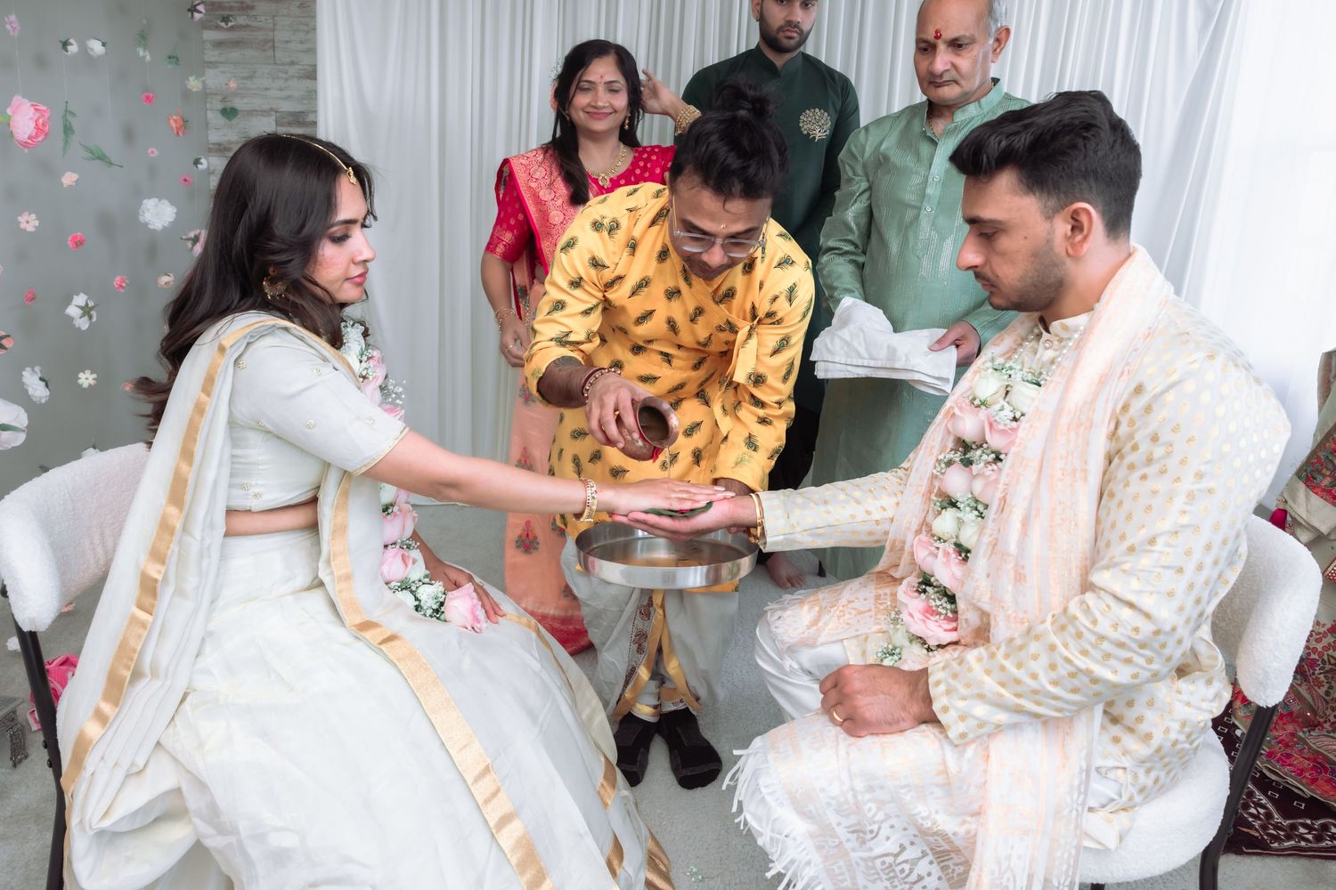 Indian wedding ritual with bride in white lehenga and groom in cream sherwani performing traditional ceremony.