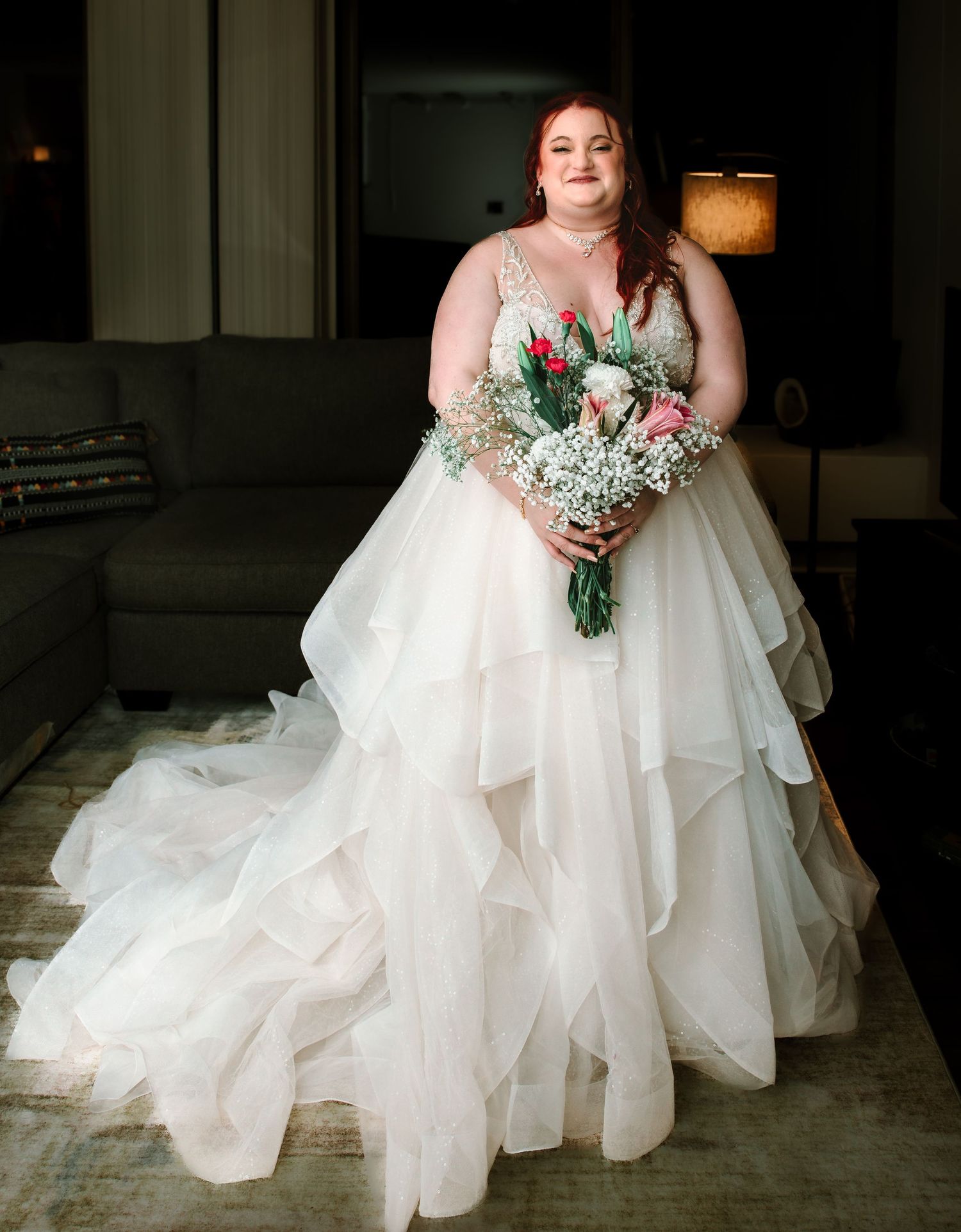 Full-length bridal portrait of red-haired bride in tiered tulle gown holding floral bouquet.