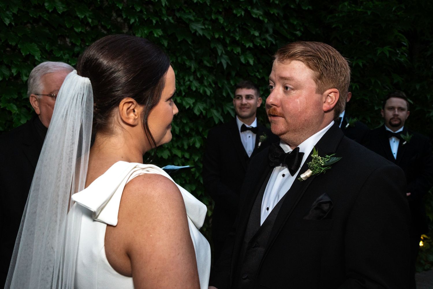 Bride and groom share an intimate moment during outdoor wedding ceremony with ivy backdrop.