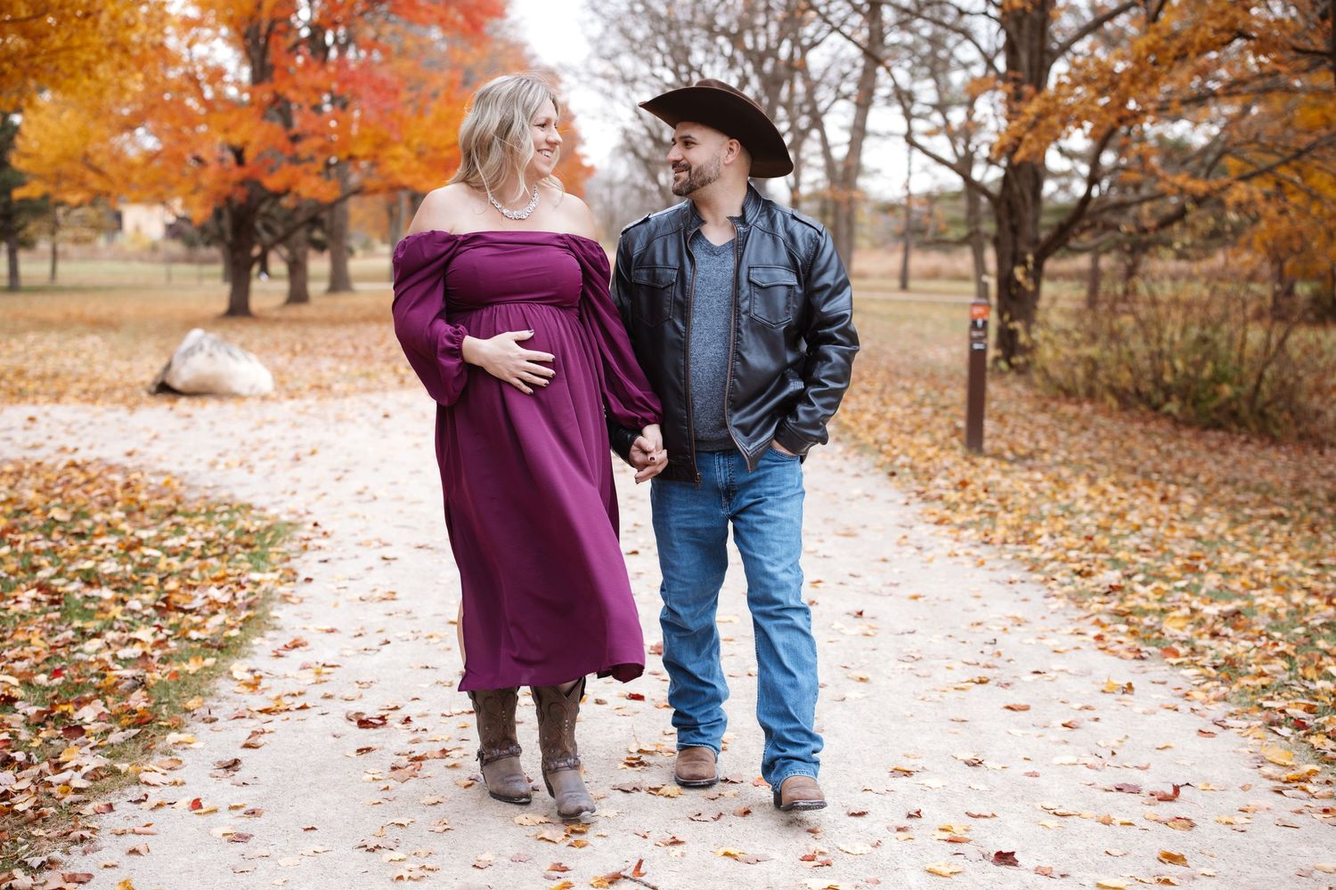 Expecting couple strolling together on a scenic autumn path lined with orange and red trees.