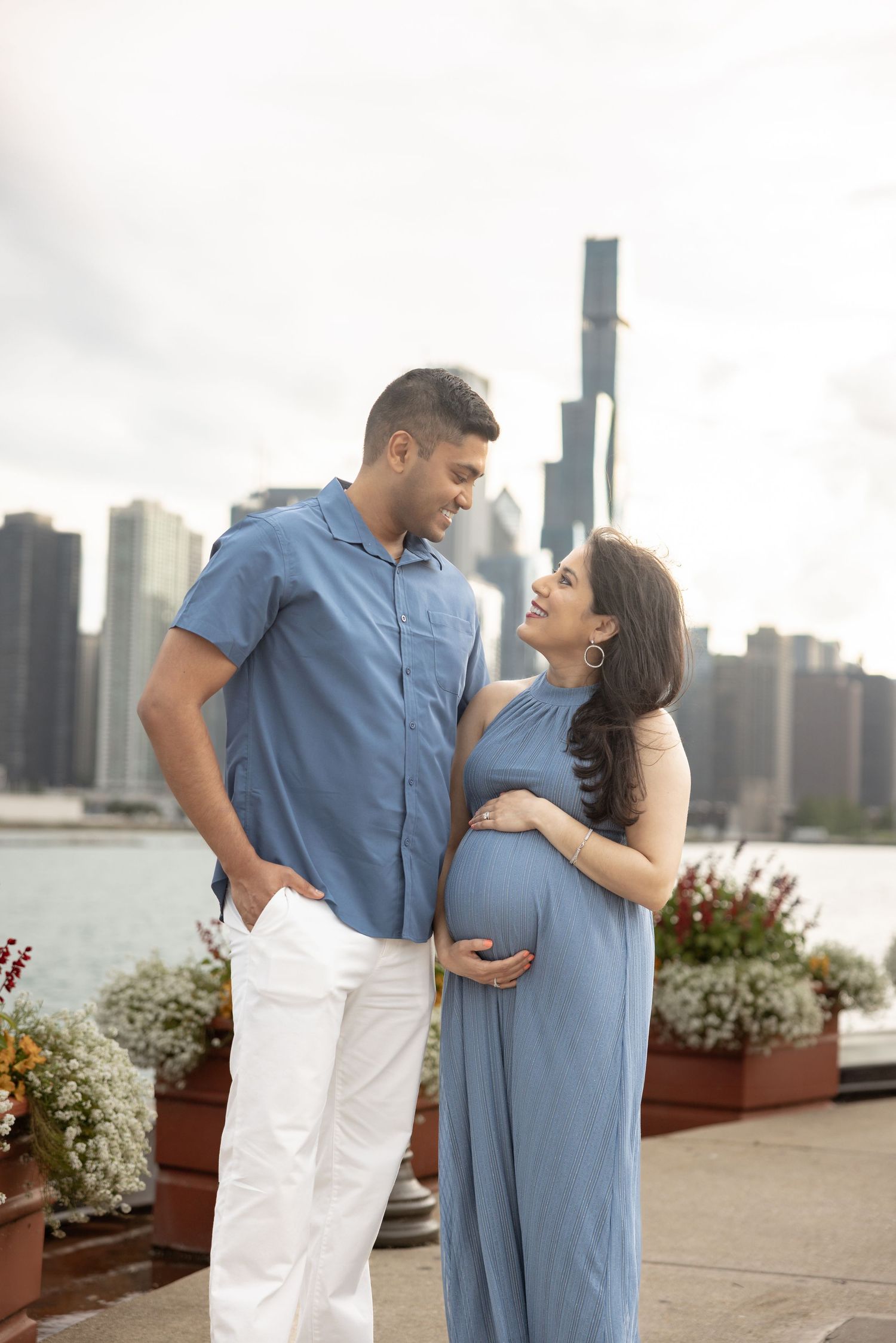 Expectant couple gazing at each other lovingly by Chicago lakefront with flowers and city skyline.