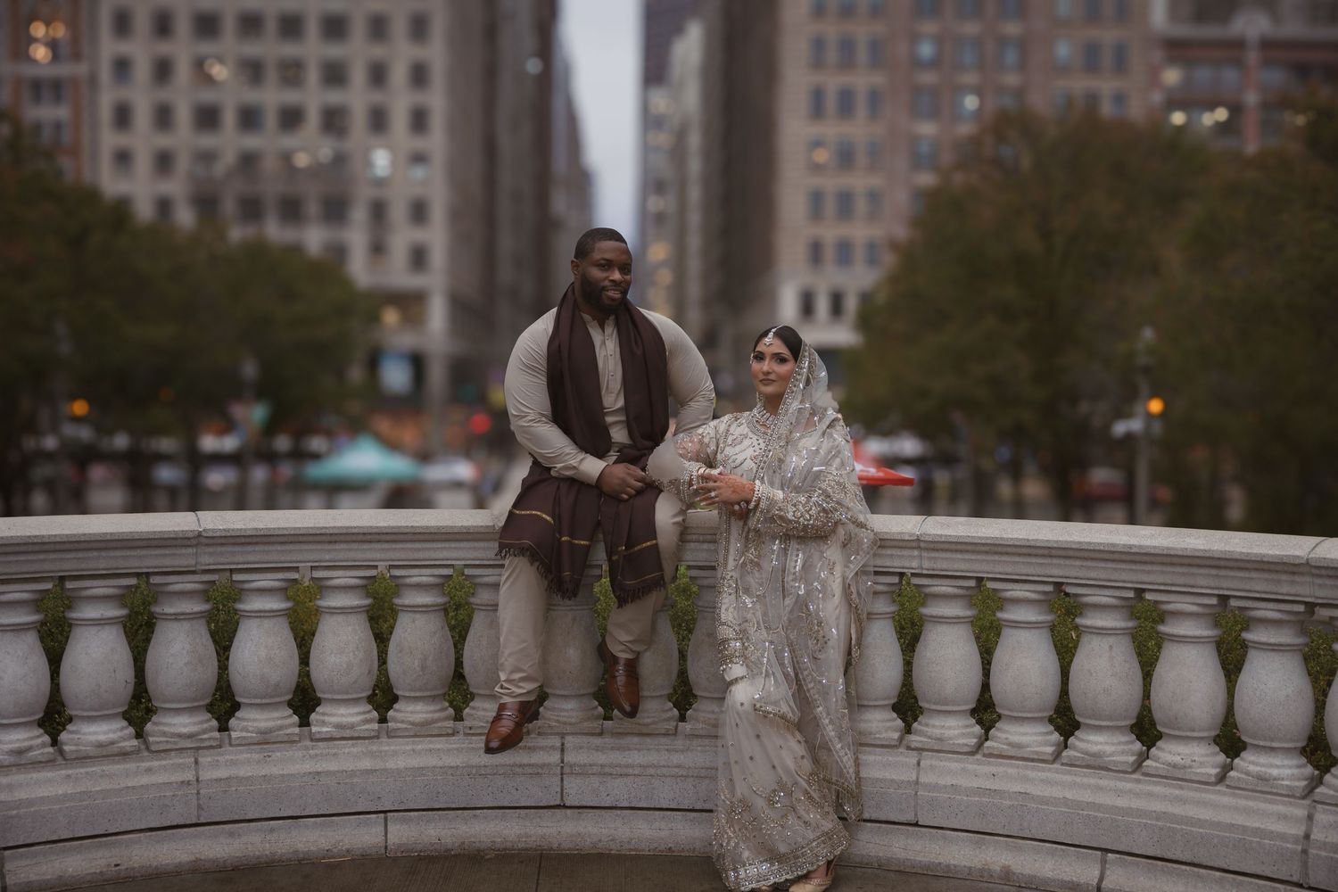 Muslim wedding couple walks on white stone bridge with urban Chicago skyline in background.