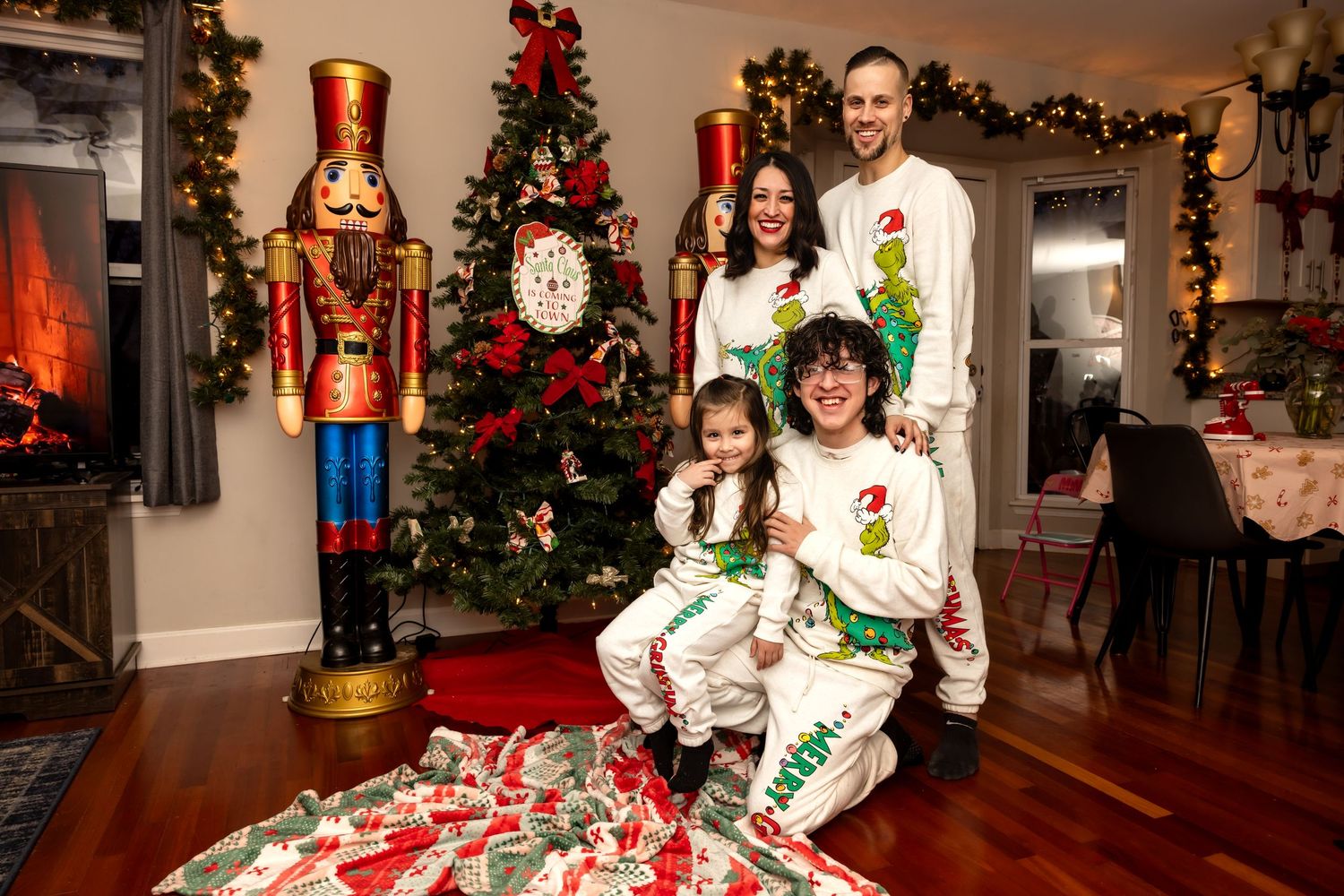 Family in matching Grinch pajamas posing by Christmas tree with nutcracker decor.