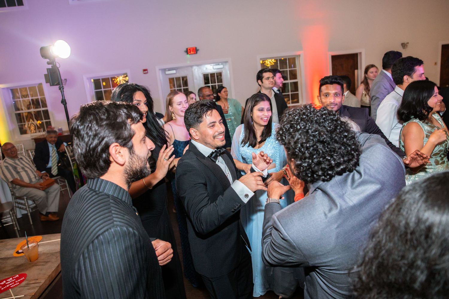 A man in a tuxedo celebrates with friends on the dance floor at a festive wedding reception.