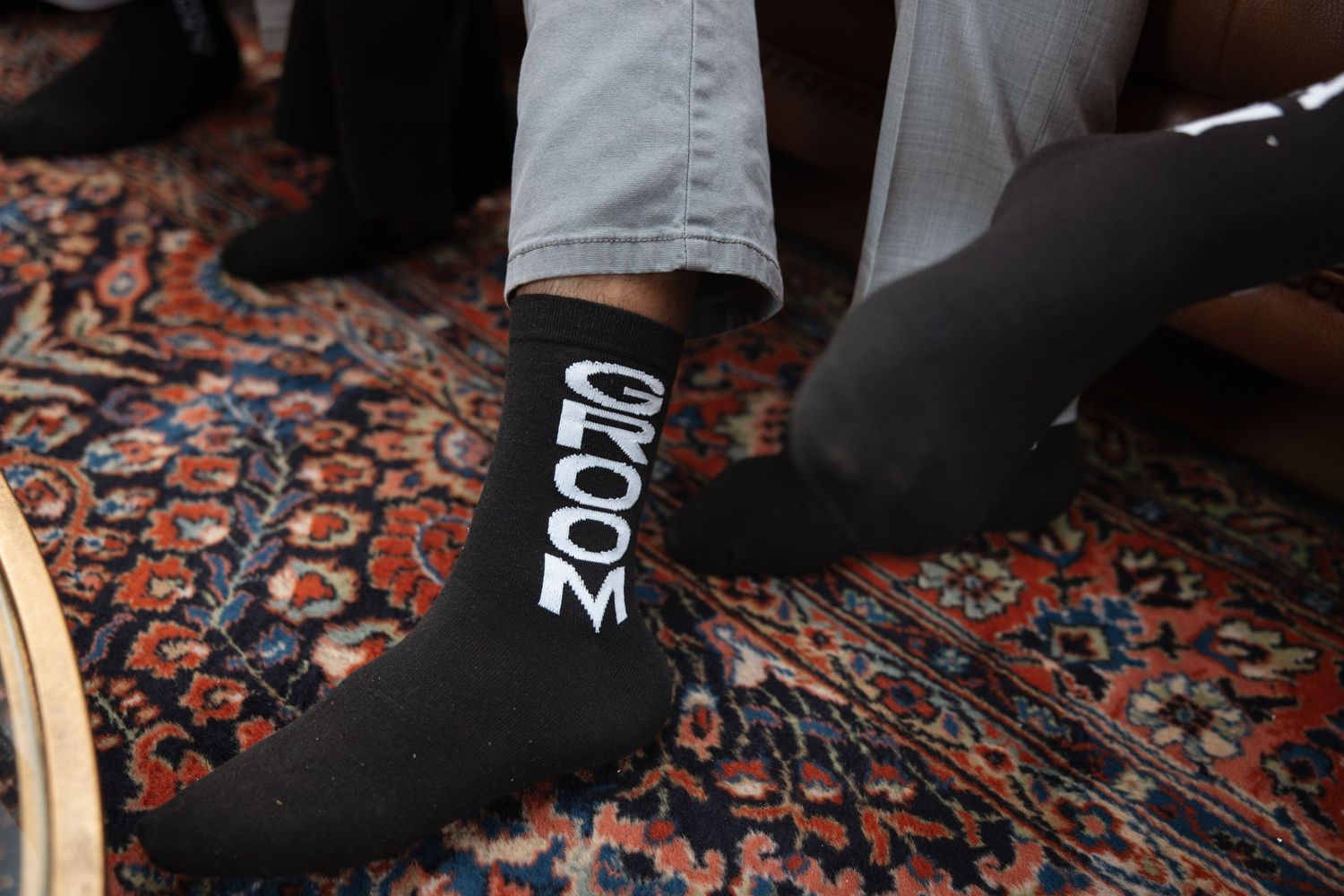 Black groom socks with white GROOM text on patterned oriental rug during wedding day preparation.