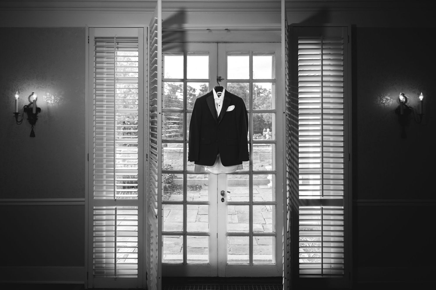Black and white photo of groom's suit hanging elegantly on French doors.